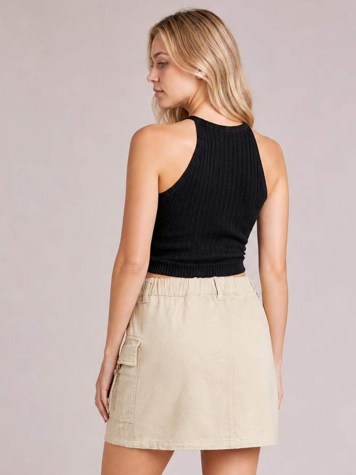 Model shown from behind wearing a beige denim mini skirt with a straight silhouette, structured waistband, visible seams, and a practical side patch pocket.