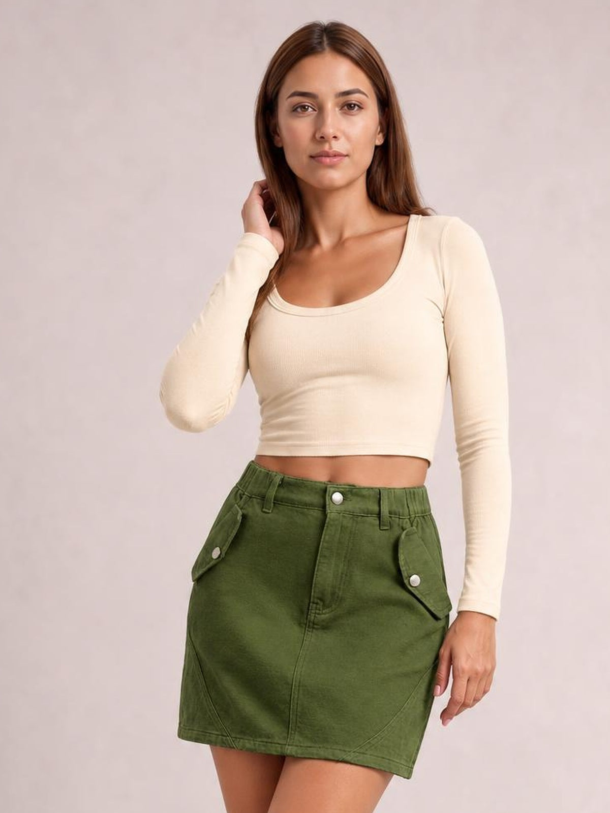 Model poses with one hand in her hair, wearing a green pocketed buttoned mini denim skirt with a straight silhouette and flap pockets.