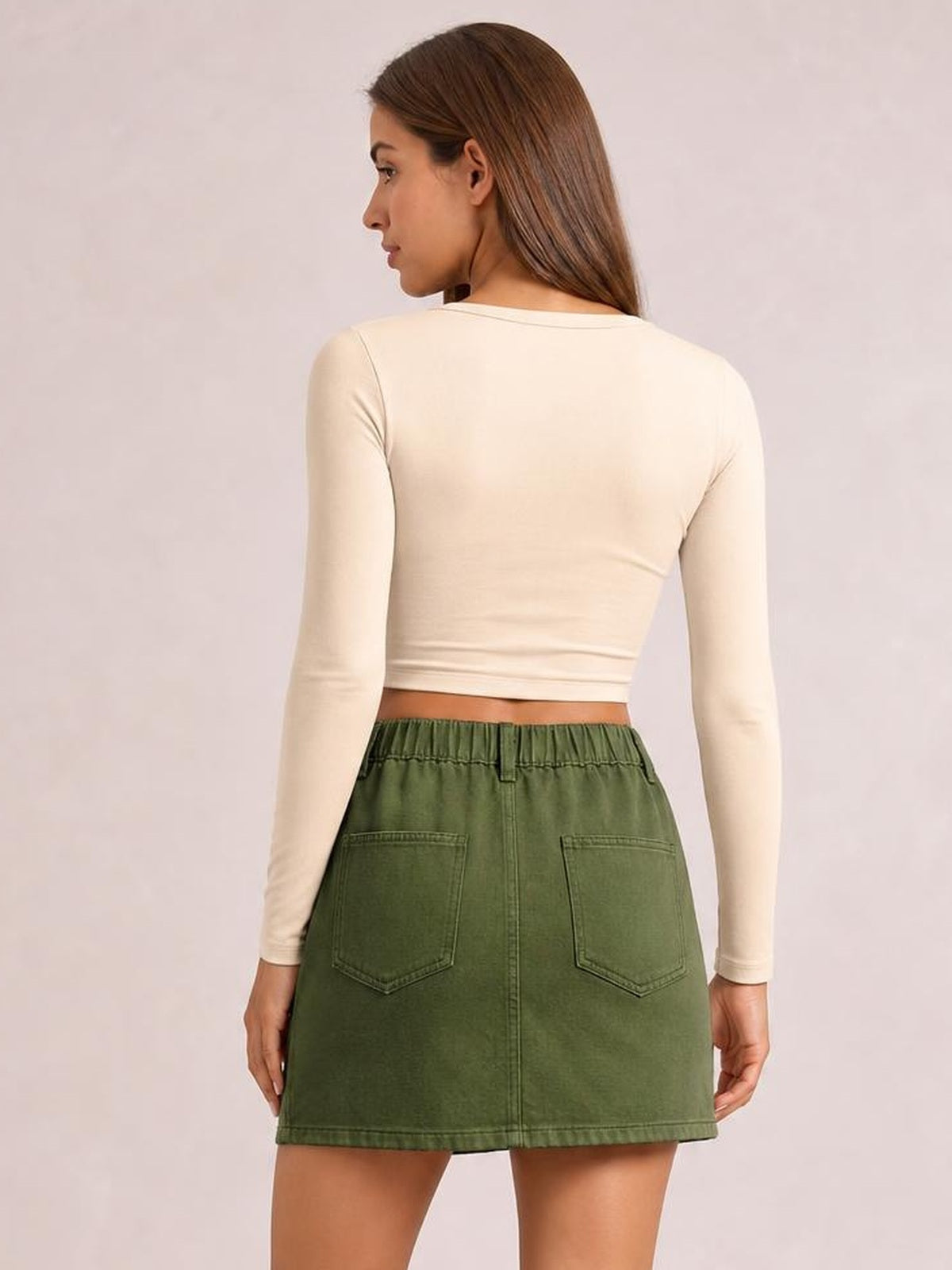 Model shown from behind wearing a green pocketed mini skirt with a straight silhouette, high waistband, twin back patch pockets, and a center back seam.