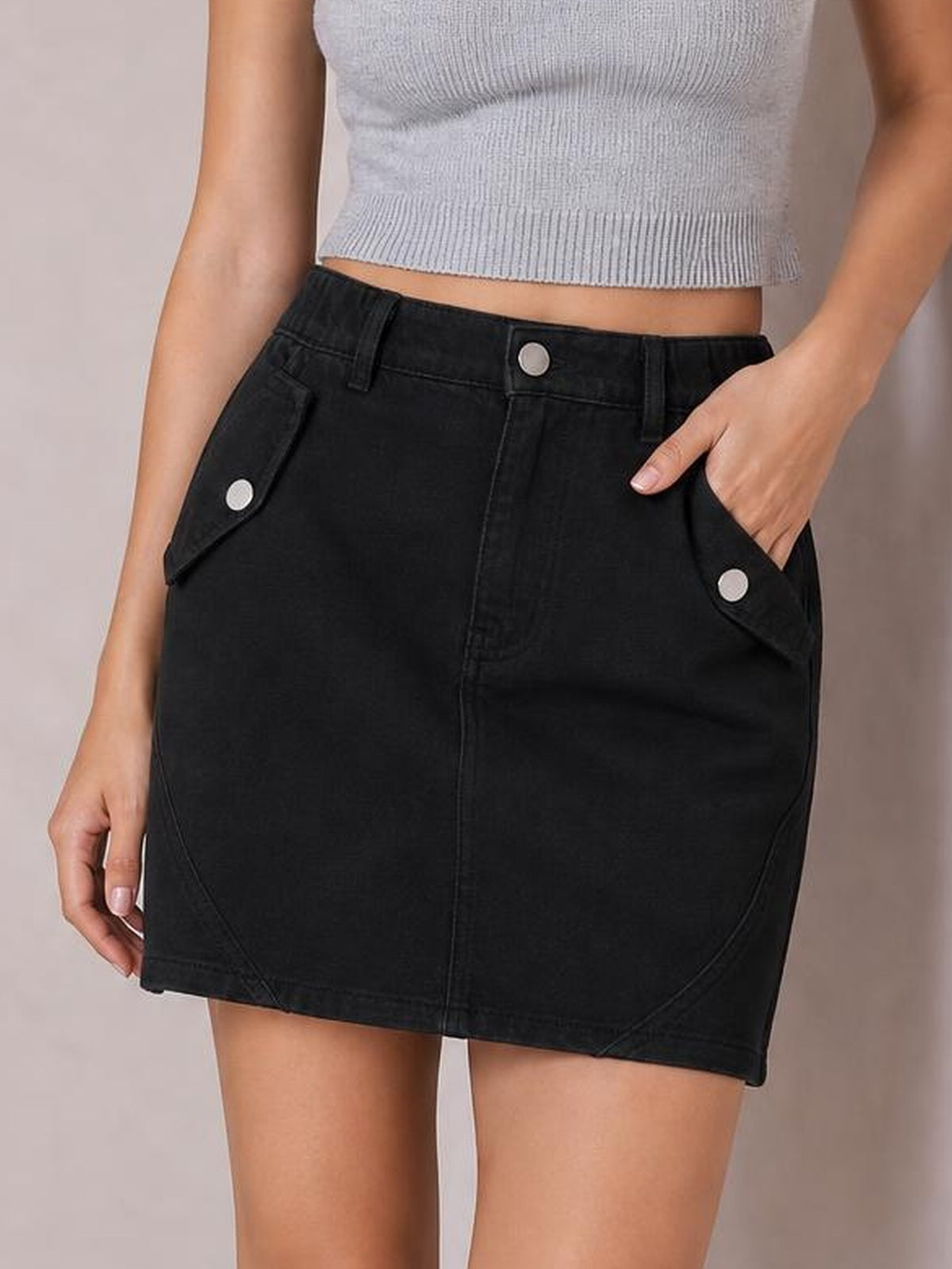 A visible model stands in a black mini denim skirt with a buttoned front, flap pockets, belt loops, curved seam details, and a straight fitted silhouette.