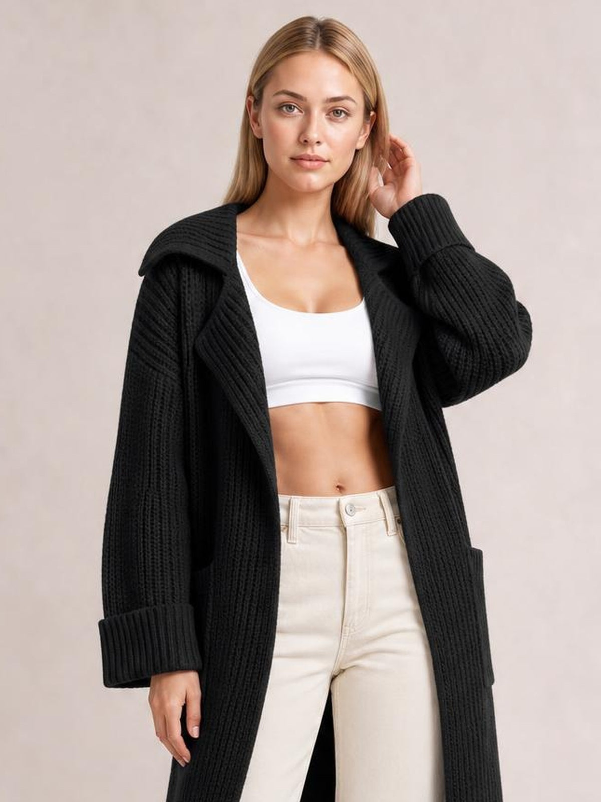 A model poses in a black ribbed cardigan with a collared neck, dropped shoulders, long sleeves, and visible front pockets, worn open over a white top.