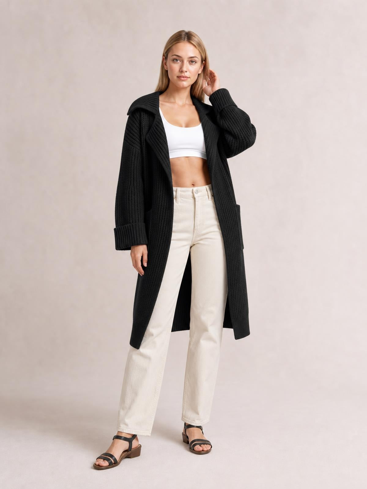 Model wearing a black ribbed pocketed collared neck cardigan with dropped shoulders, long relaxed silhouette, and rolled cuffs over a white top.