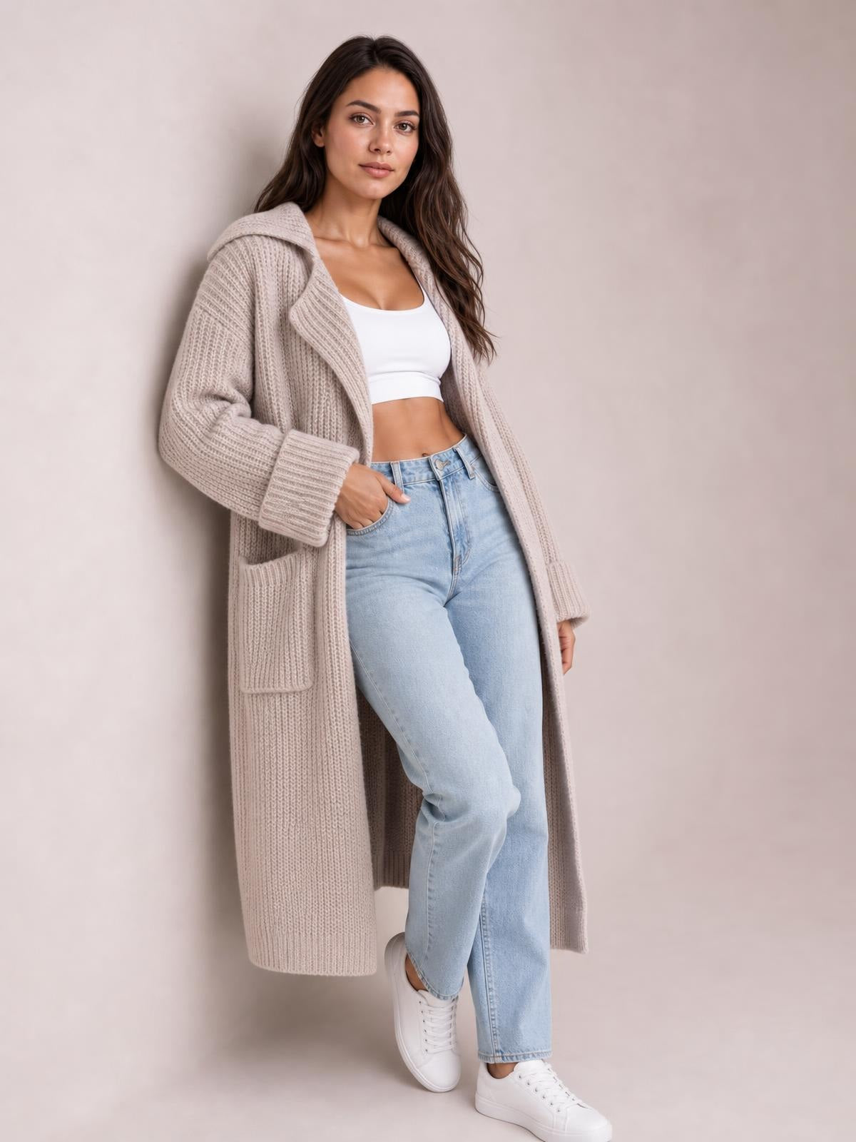 A model poses in a light taupe rib-knit cardigan with a collared neck, dropped shoulders, longline silhouette, patch pockets, and wide cuffs.