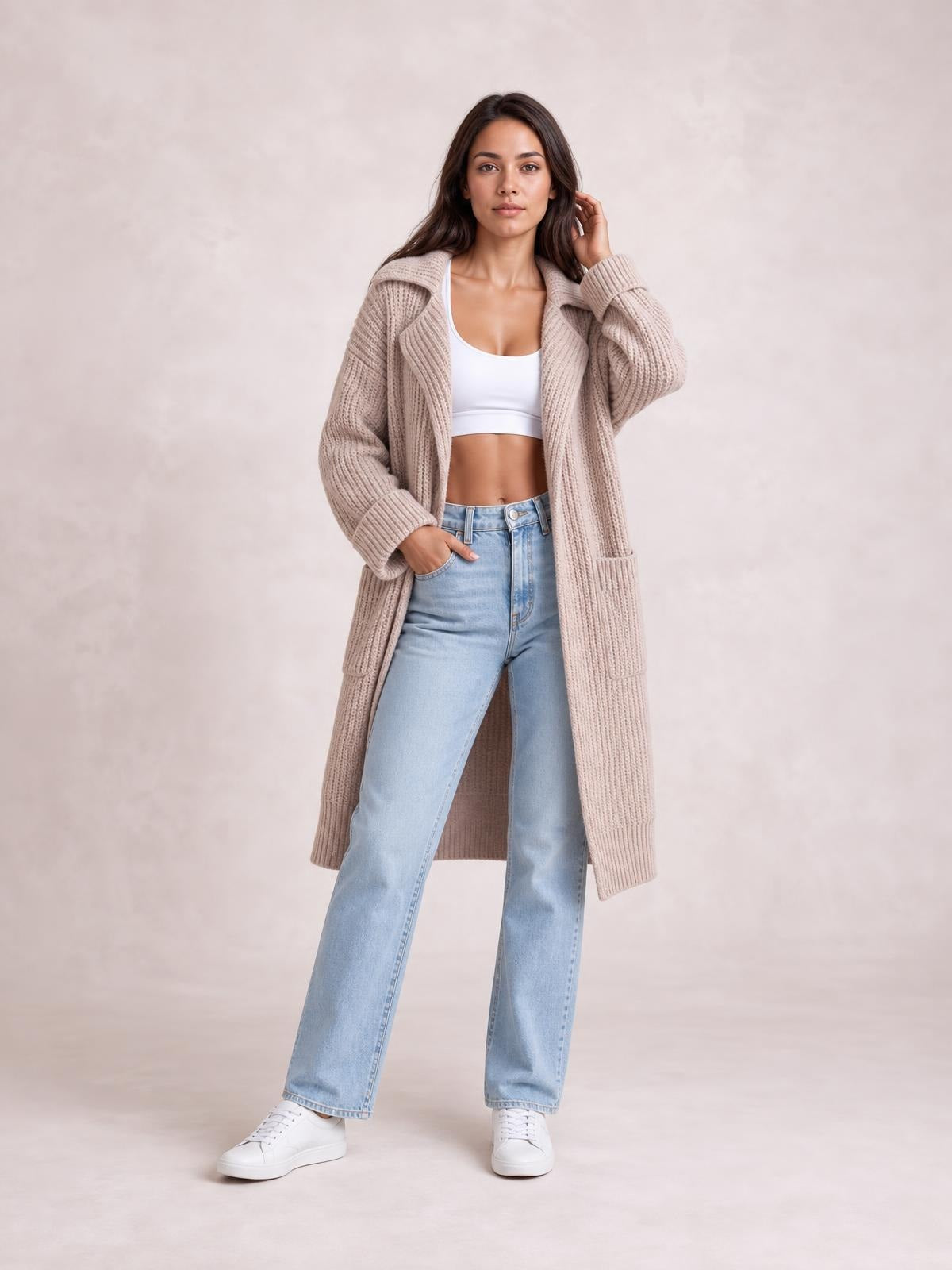 A model wears a taupe longline cardigan with a collared neck, dropped shoulders, ribbed knit texture, oversized sleeves, and front patch pockets.