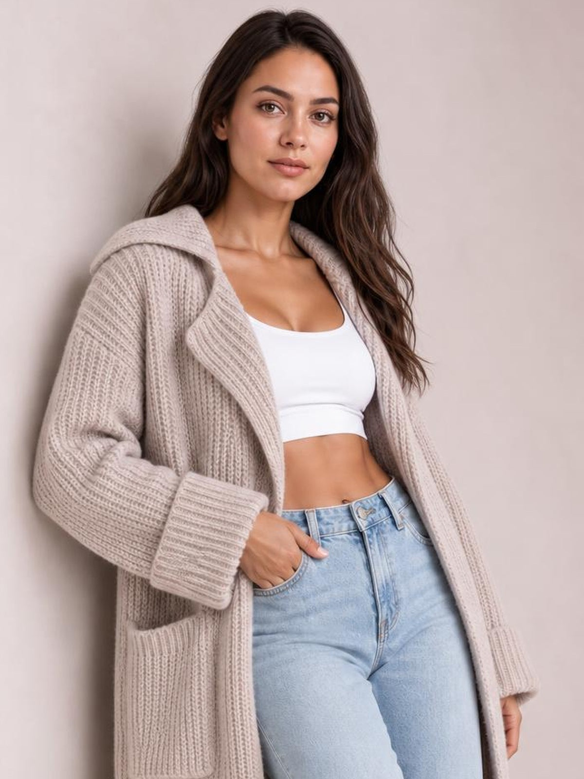 A model poses in a relaxed taupe cardigan with a collared neckline, dropped shoulders, chunky ribbed knit, long sleeves, open front, and patch pockets.