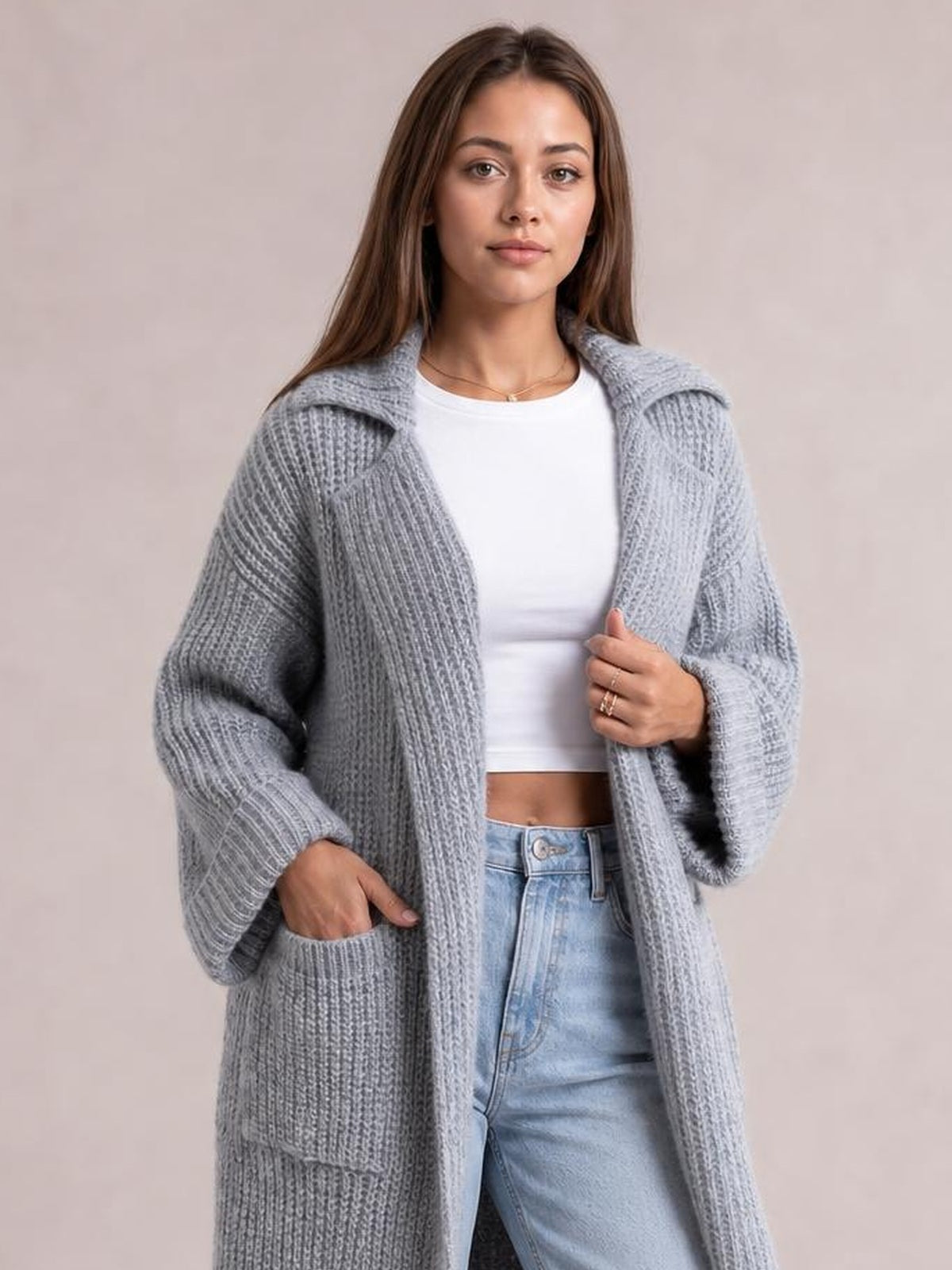 Model wearing a light gray ribbed cardigan with a collared neck, dropped shoulders, relaxed long silhouette, and large patch pockets, holding the front edge.