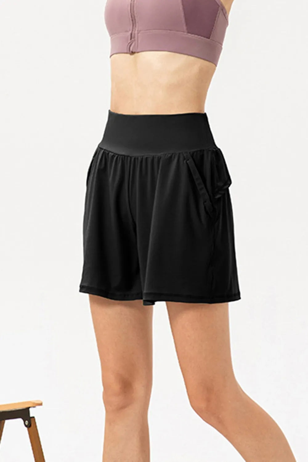 A model poses in black pocketed active shorts with an elastic waistband, relaxed loose silhouette, gathered side panels, and lightweight curved hems.