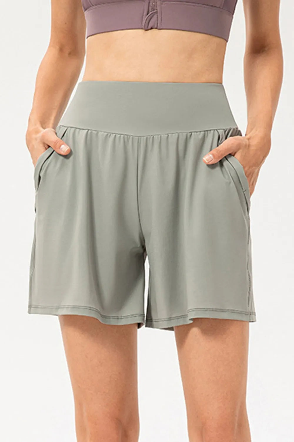 A model wears sage green active shorts with an elastic waist, relaxed wide-leg silhouette, side pockets, moderate stretch, and neatly stitched hems.
