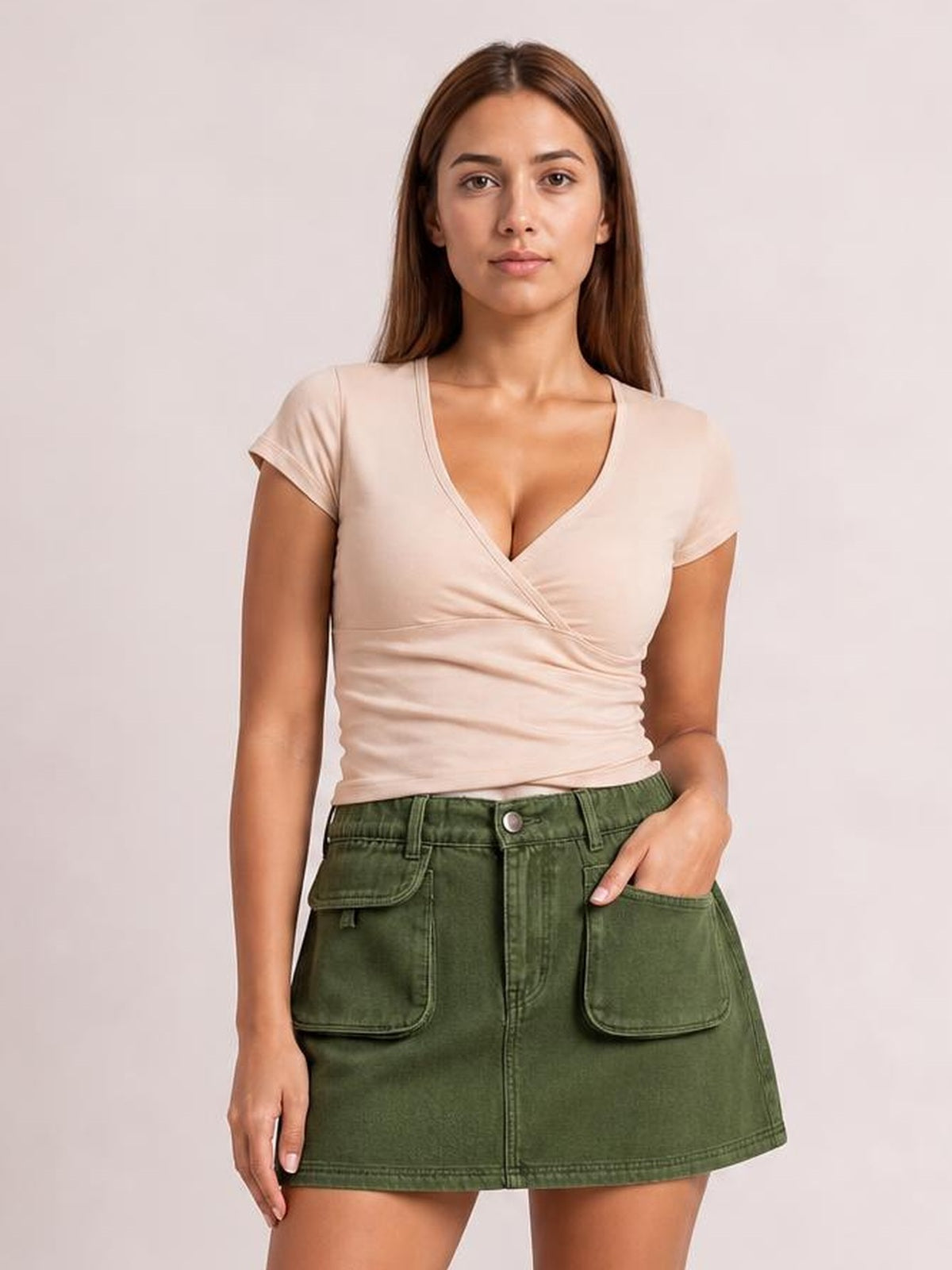 A model wears an olive green denim mini skirt with an elastic waist, buttoned front, large patch pockets, and a structured A-line silhouette.