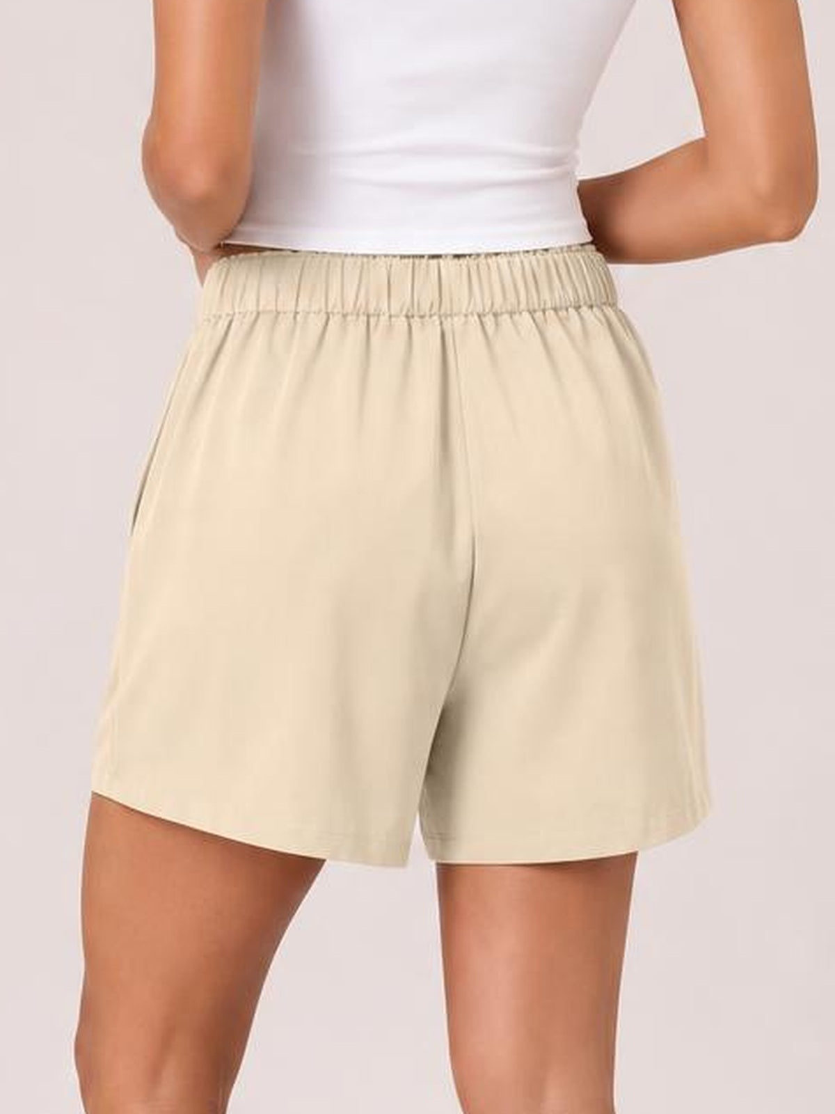 Model shown from the back in beige pocketed shorts with a ruched half-elastic waistband and relaxed, straight-leg silhouette.