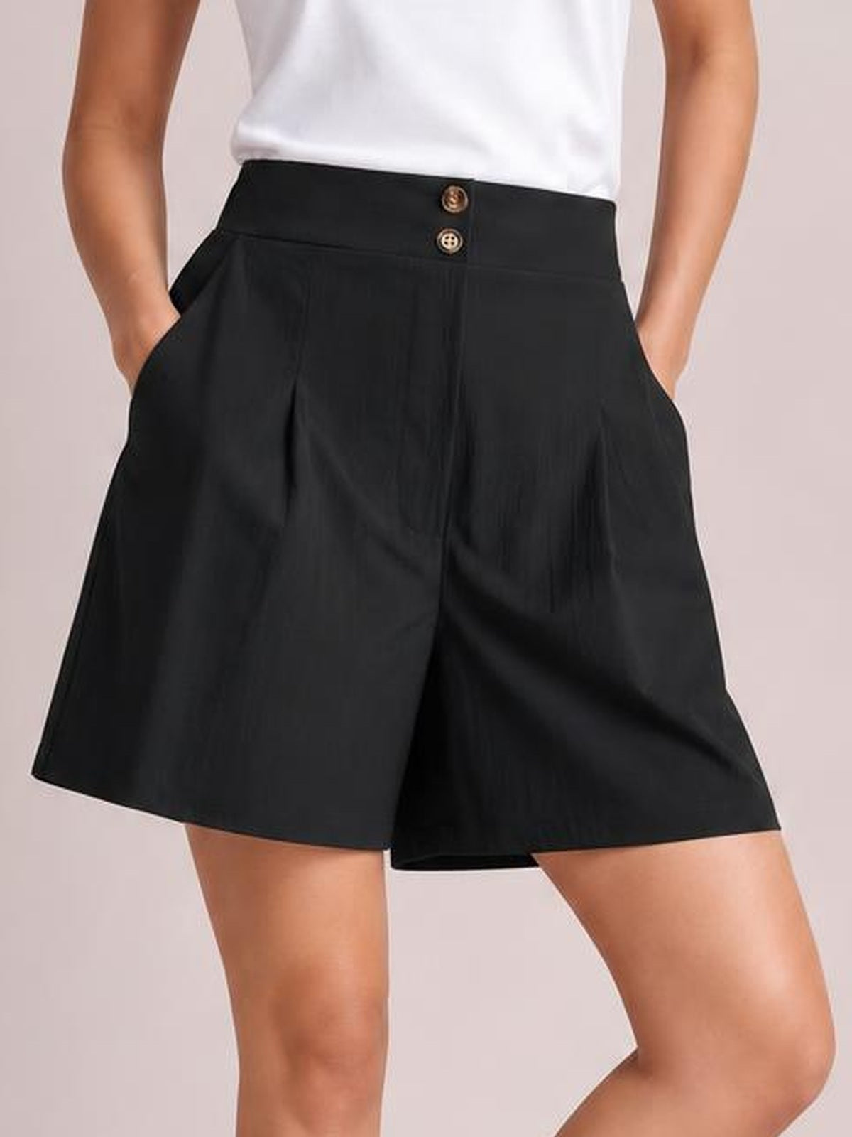 Model wearing black pocketed shorts with a high half-elastic waist, button-front waistband, relaxed wide-leg silhouette, and hands tucked into the side pockets.