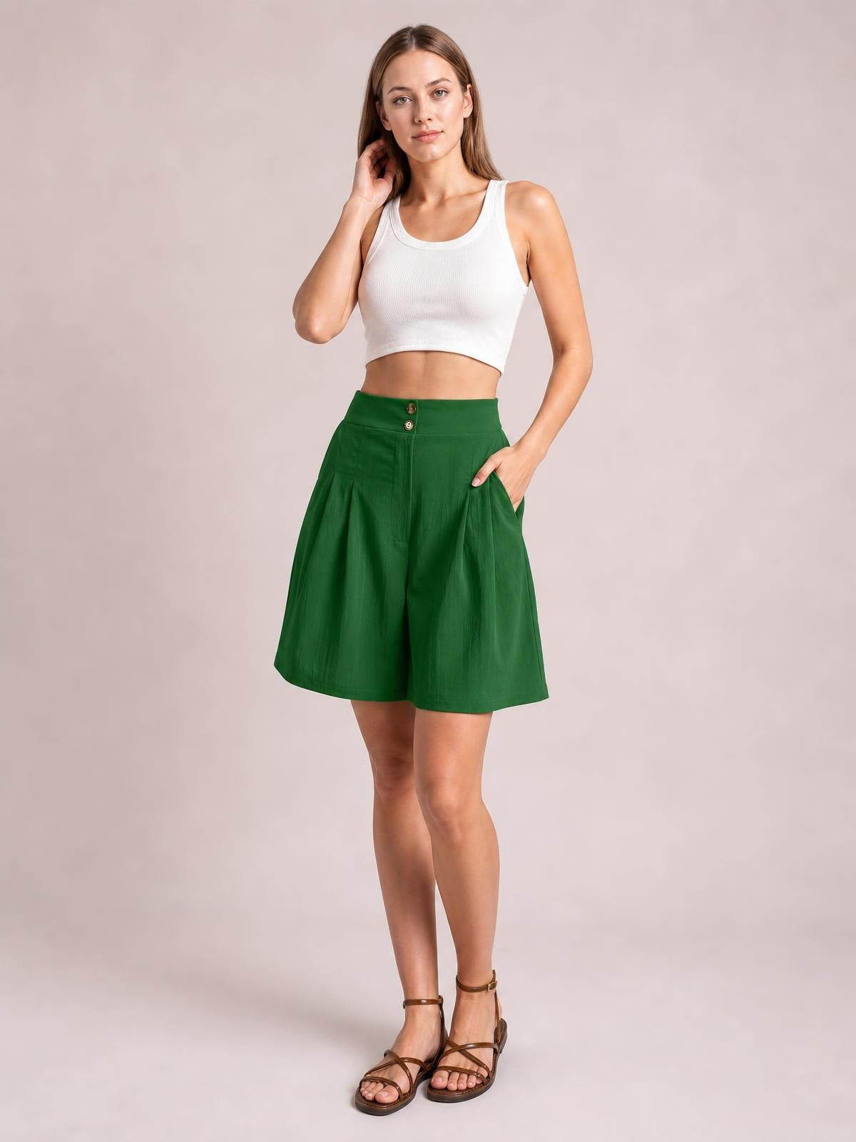 Model poses with one hand in the pocket of green high-waisted shorts featuring a button front, half elastic waist, and relaxed wide-leg silhouette.