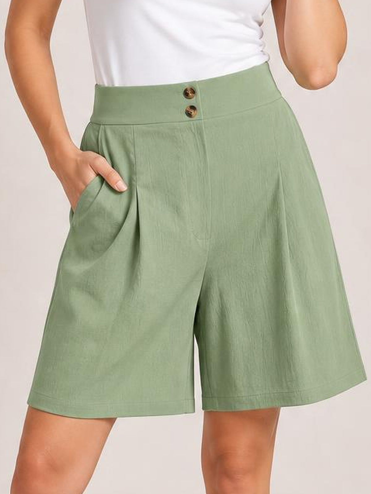Model wears sage green pocketed shorts with a high-rise half-elastic waistband, front buttons, subtle ruching, and a relaxed wide-leg silhouette.