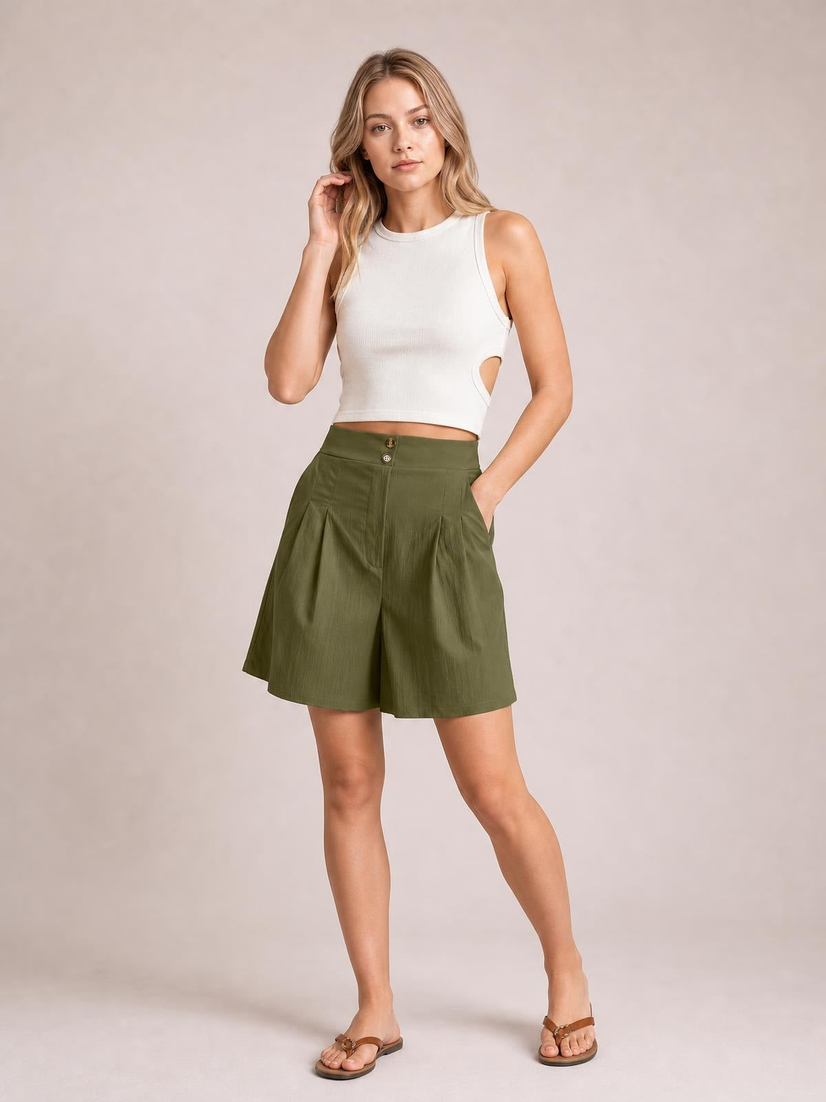 Model poses in olive green pocketed shorts with a high waistband, button closure, front pleats, and a relaxed wide-leg silhouette.