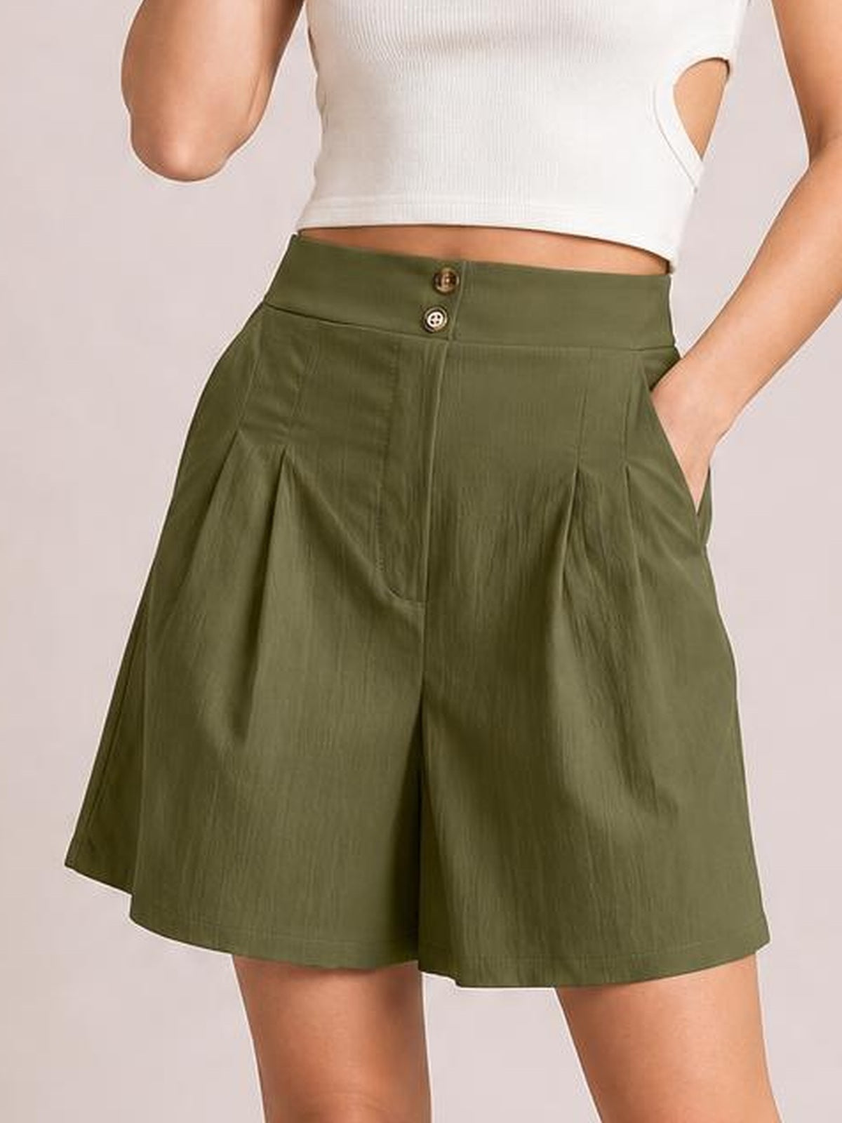 A model wears olive green pocketed shorts with a half-elastic waistband, button fly, front pleats, and a relaxed wide-leg silhouette, hands in pockets.