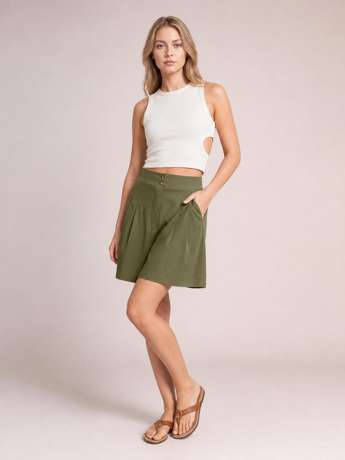 A model poses in olive-green pocketed shorts with a buttoned front, relaxed wide-leg silhouette, and subtle ruching, one hand in a pocket.