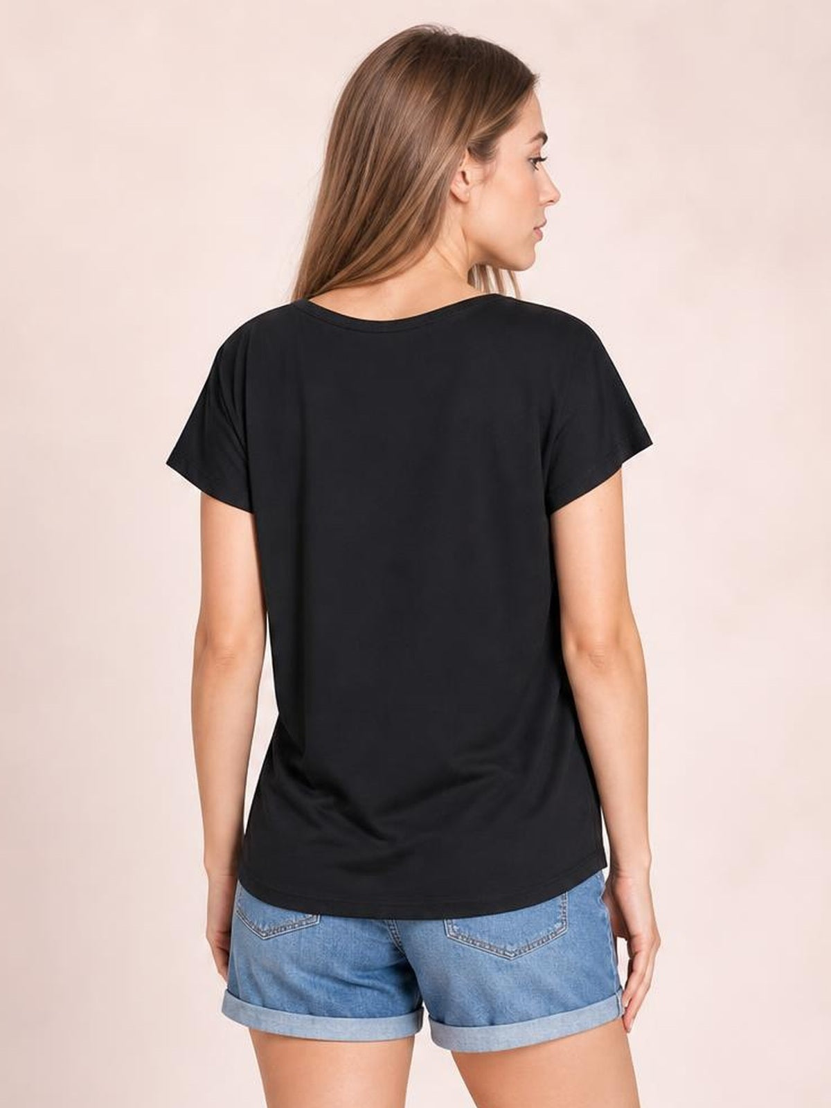 A woman models the black short-sleeve T-shirt from the back, showing its relaxed silhouette, smooth construction, and curved hem.