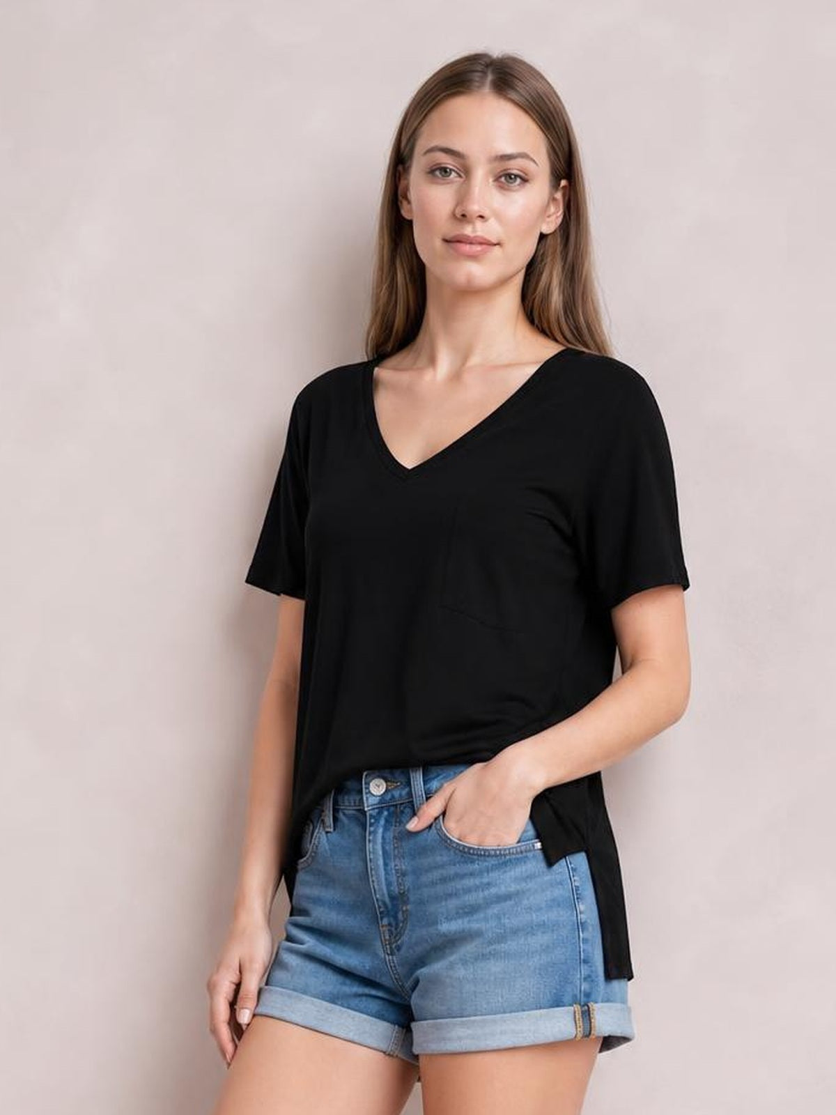 Model wearing a black pocketed heathered V-neck short sleeve T-shirt with a relaxed, slightly longer silhouette, standing with one hand in her shorts pocket.
