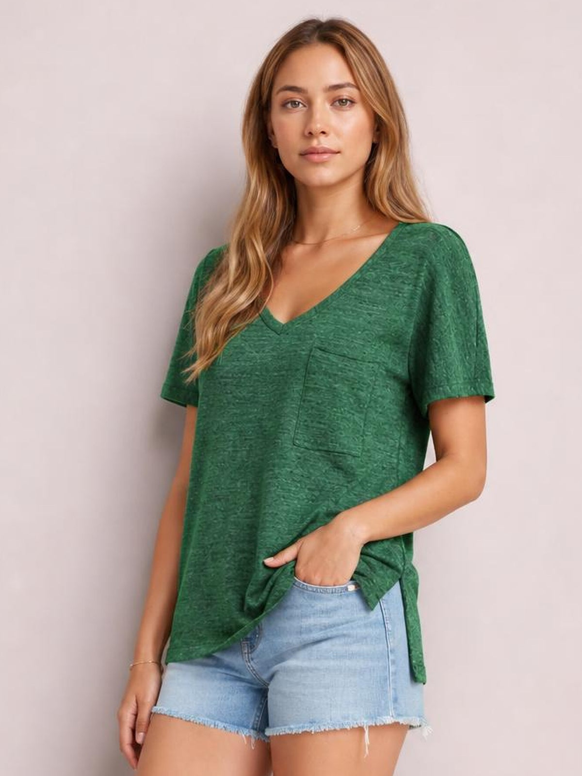 A model wears a green heathered V-neck short sleeve T-shirt with a chest patch pocket and relaxed, slightly loose silhouette.