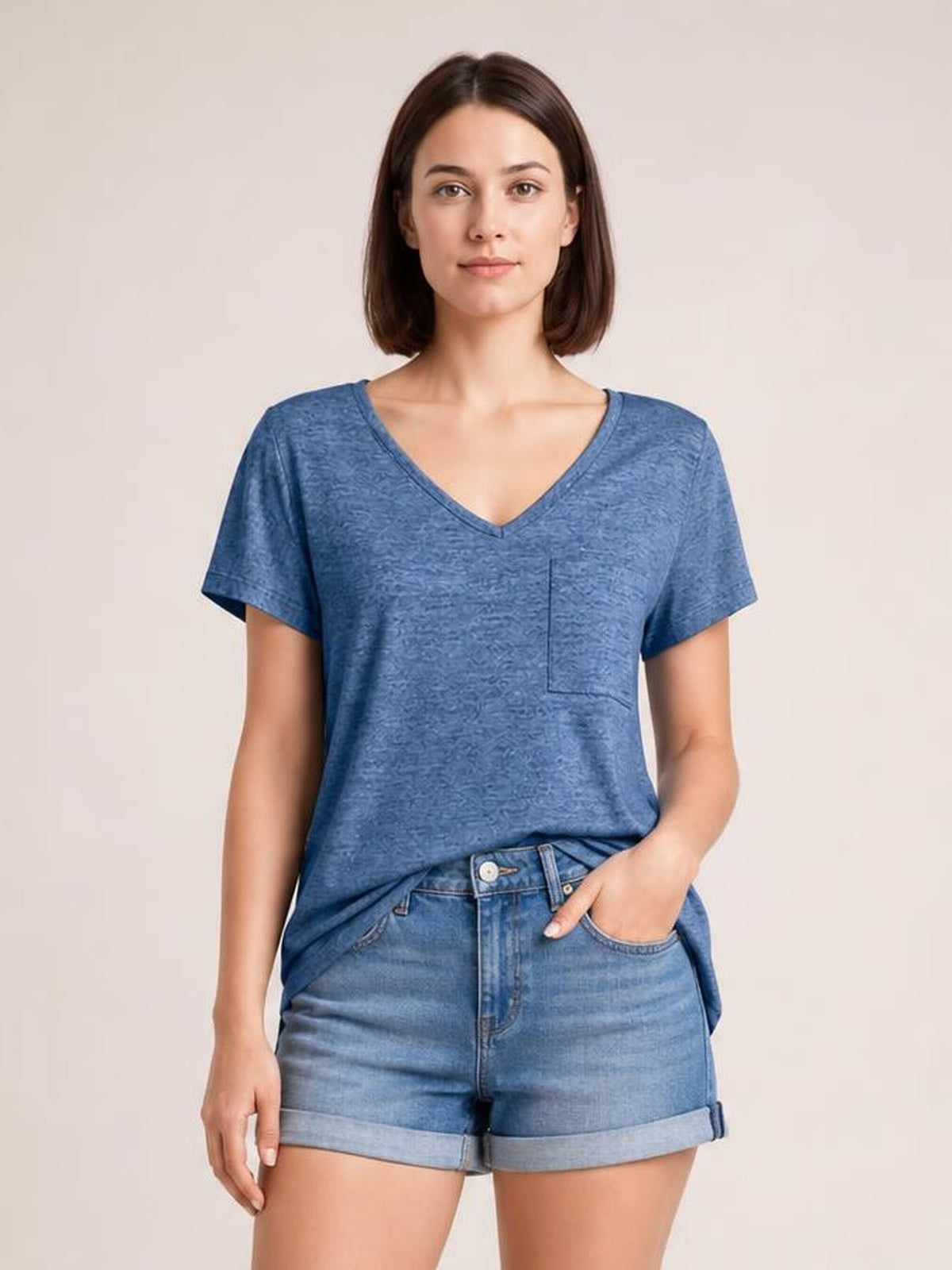 Model wears a blue heathered short-sleeve T-shirt with a V-neck, chest pocket, and relaxed straight silhouette, posing with one hand in her shorts pocket.