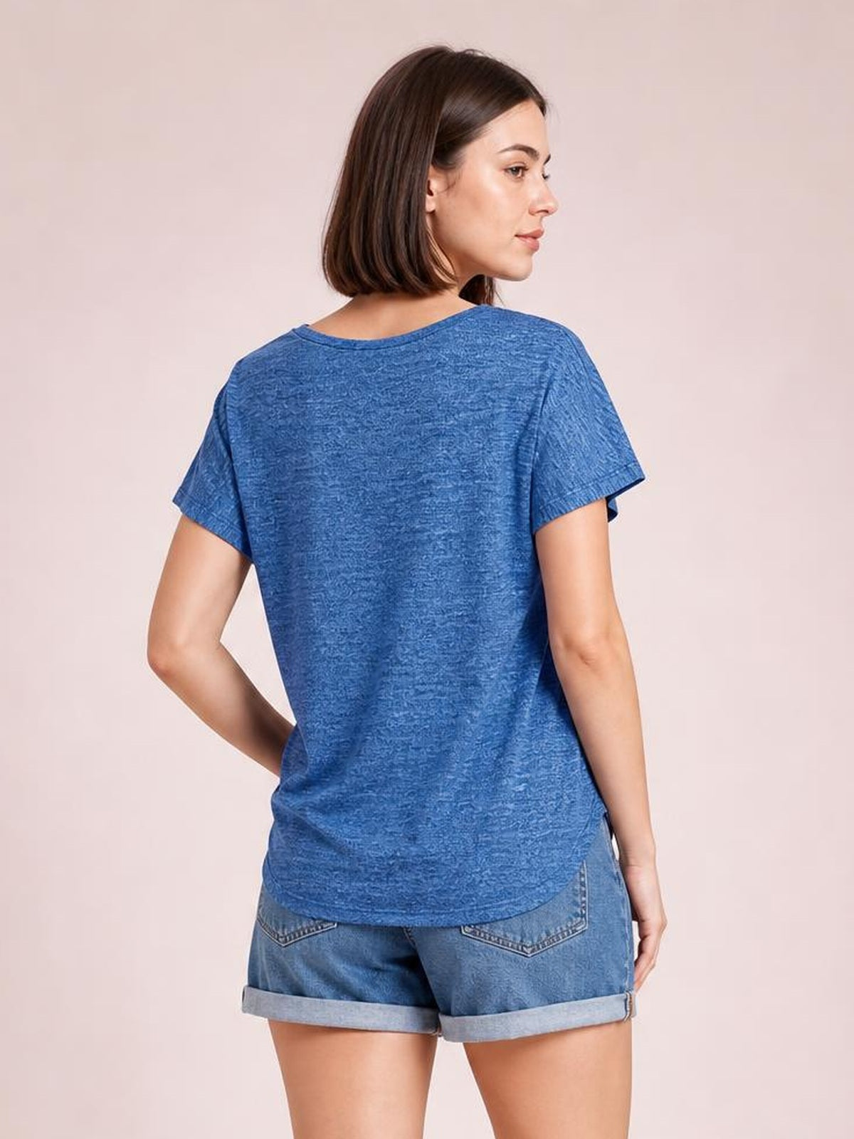 Model shown from the back in a blue heathered short-sleeve T-shirt with a relaxed silhouette and curved hem, resting one hand at her hip.