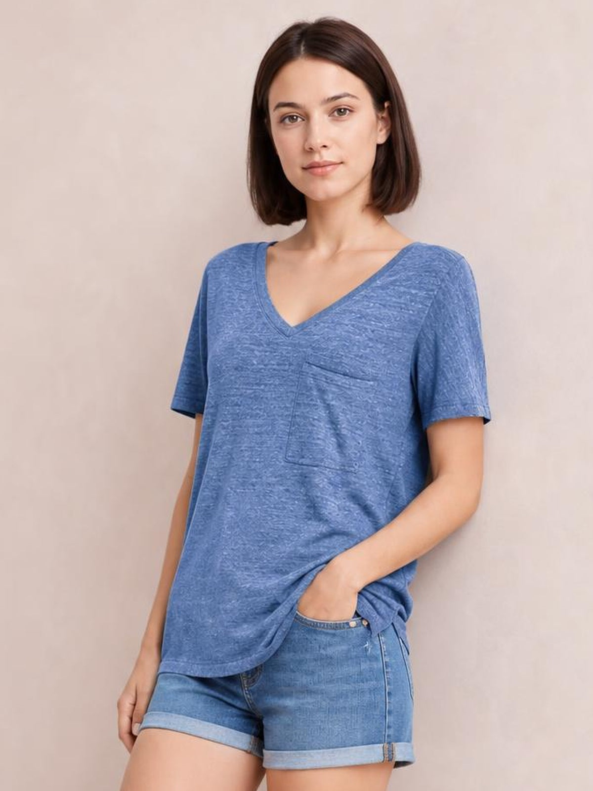 Model wears a blue heathered V-neck short sleeve T-shirt with a relaxed silhouette and front pocket, posing with one hand in her shorts pocket.