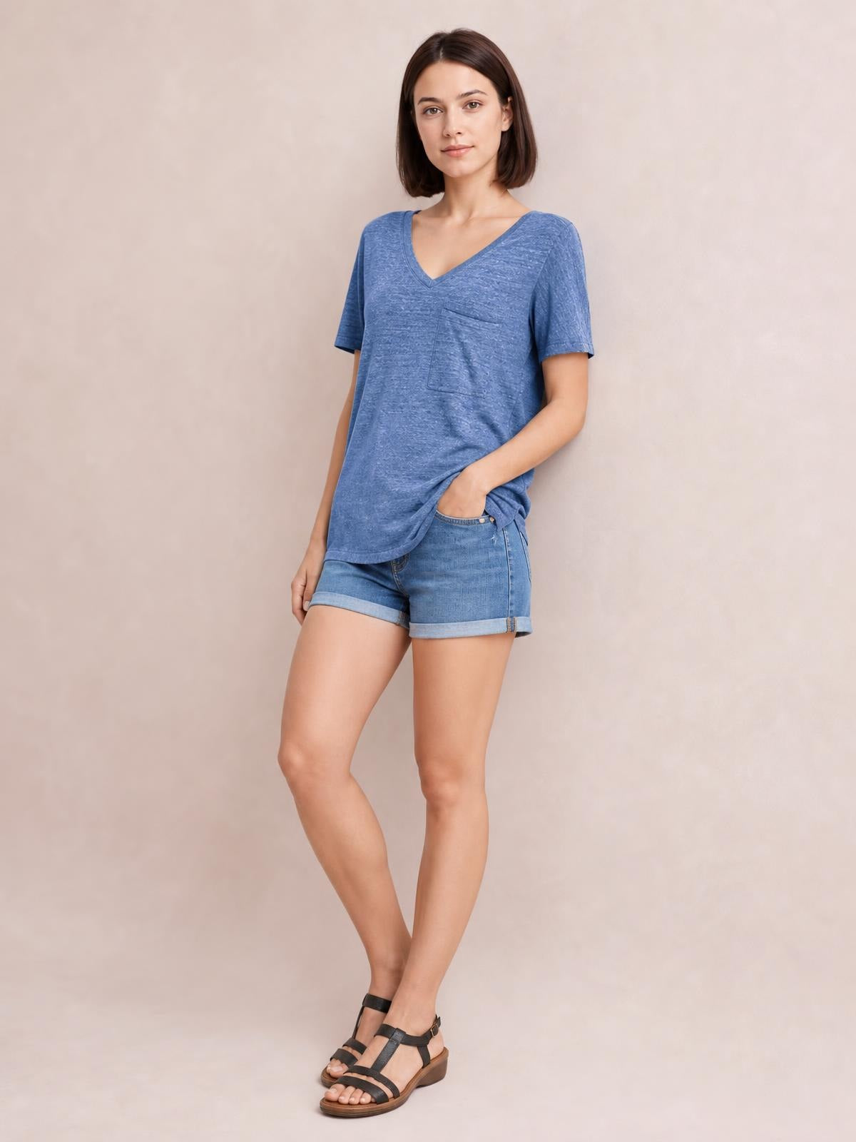 Model poses in a blue heathered V-neck short sleeve T-shirt with a chest pocket and relaxed silhouette, paired with denim shorts.