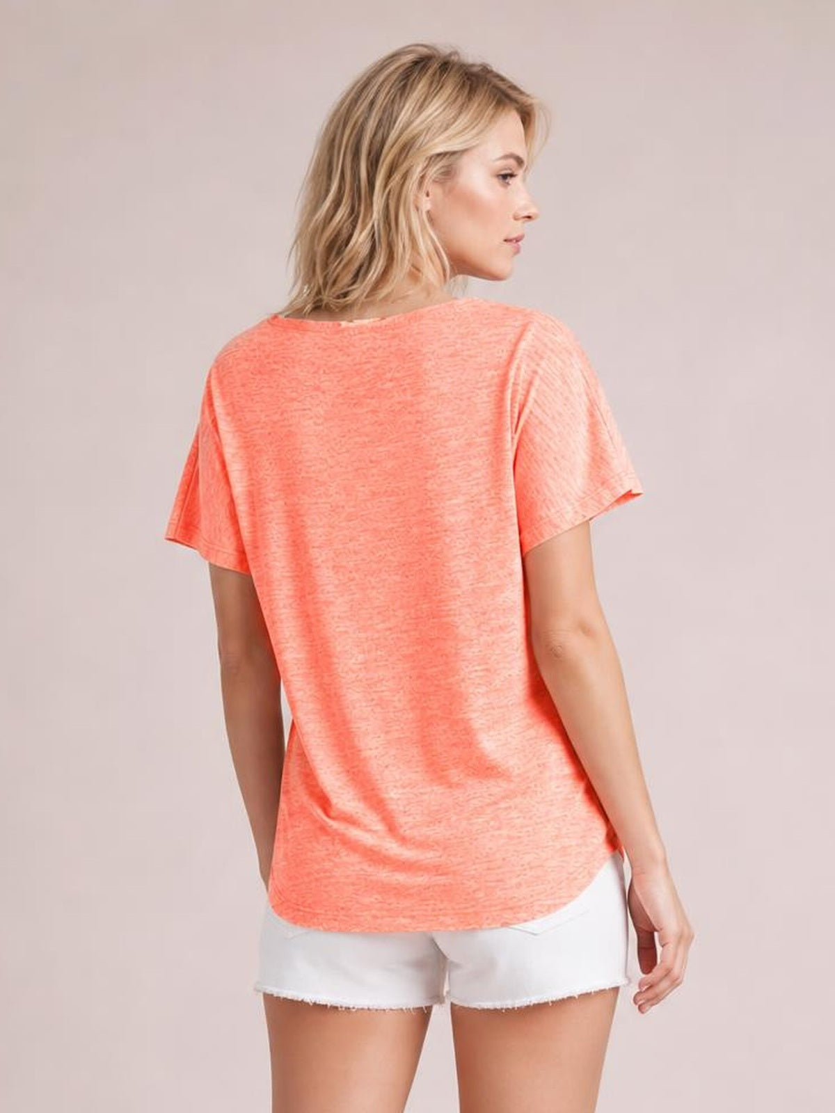 Model shown from the back wearing a coral heathered short-sleeve T-shirt with a relaxed silhouette, curved hem, and softly draped construction.
