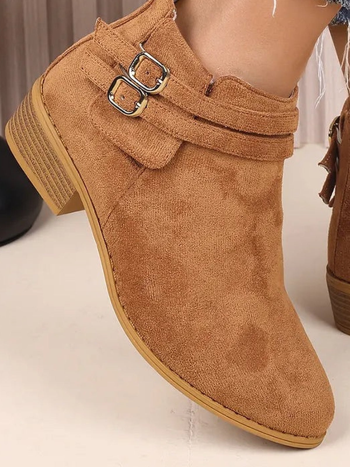 A tan suede point-toe ankle boot features a sleek silhouette, double buckle straps, a low block heel, and a durable rubber sole.