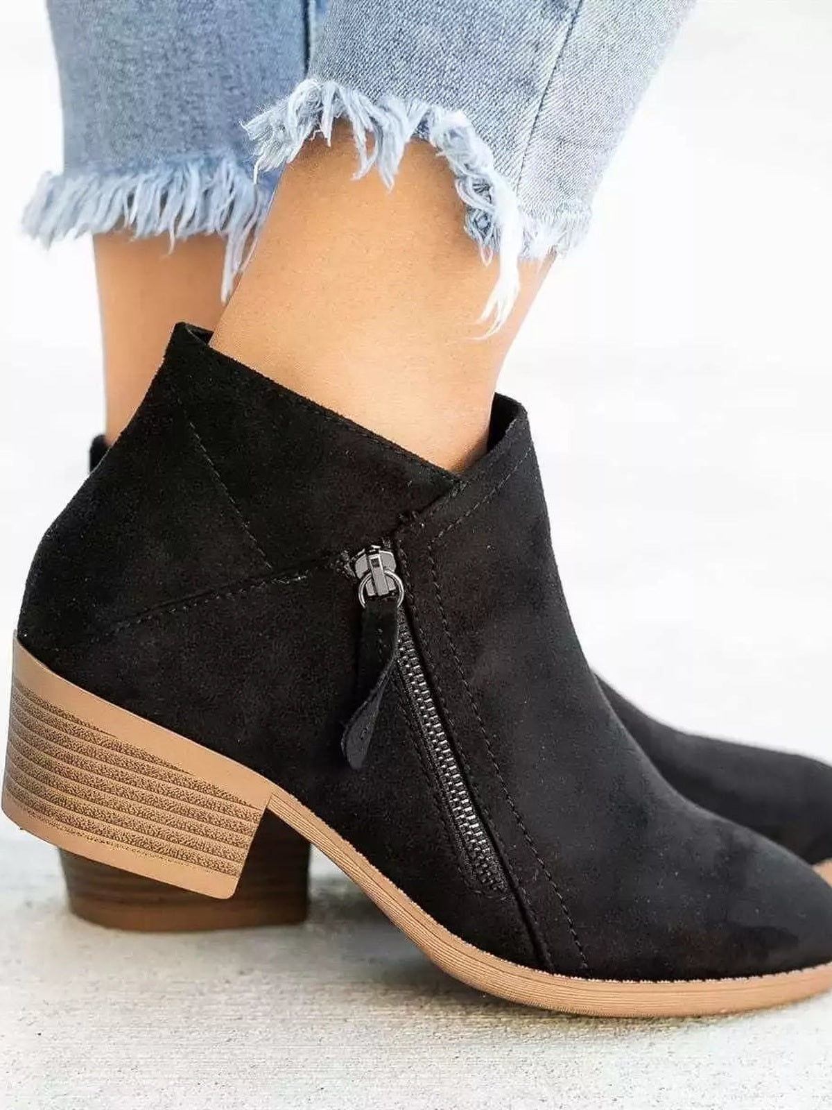 A model wears black point toe block heel ankle boots with side zippers, textured tan soles, and sturdy low heels beneath cuffed distressed jeans.