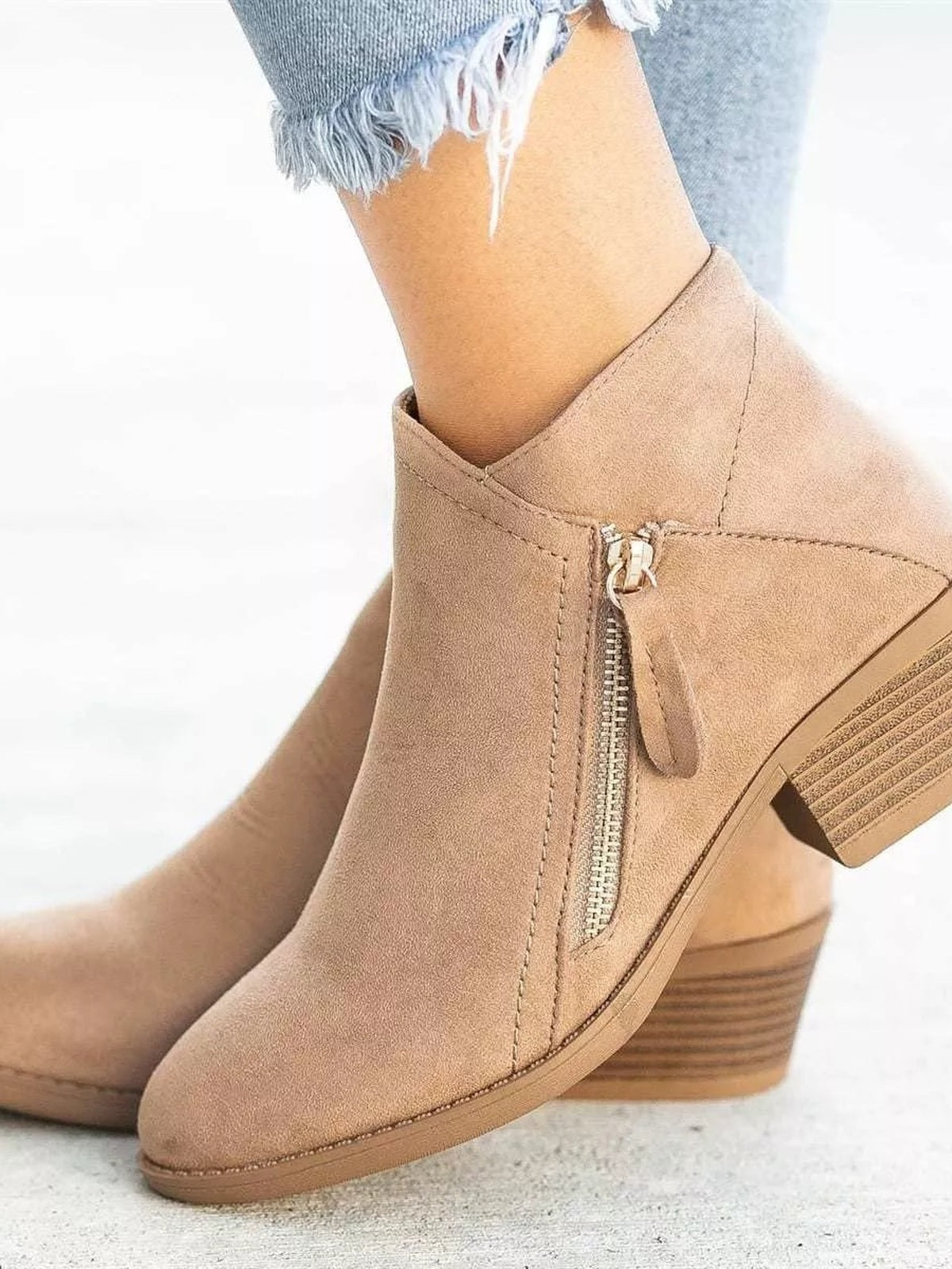 A model wears tan point-toe ankle boots with side zippers, stitched panels, smooth uppers, and sturdy stacked block heels while standing.