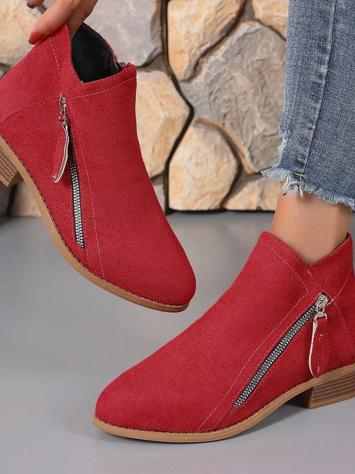 Red ankle boots with side zippers, pointed toes, low block heels, and stitched uppers are shown on a model wearing cropped frayed jeans.