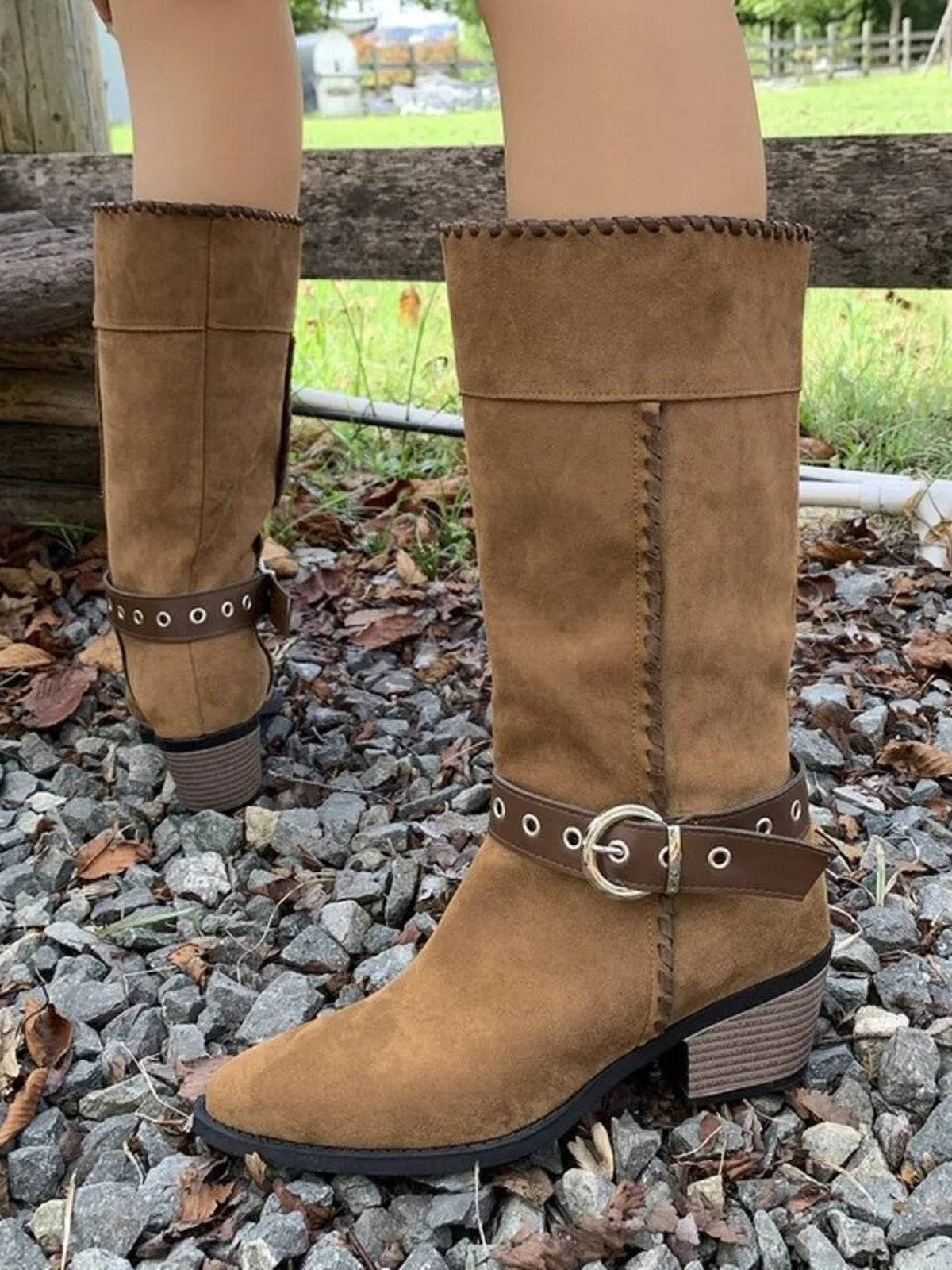 A model wears tan PU leather point-toe boots with mid block heels, tall shafts, stitched trim, and buckled ankle straps with metal eyelets.