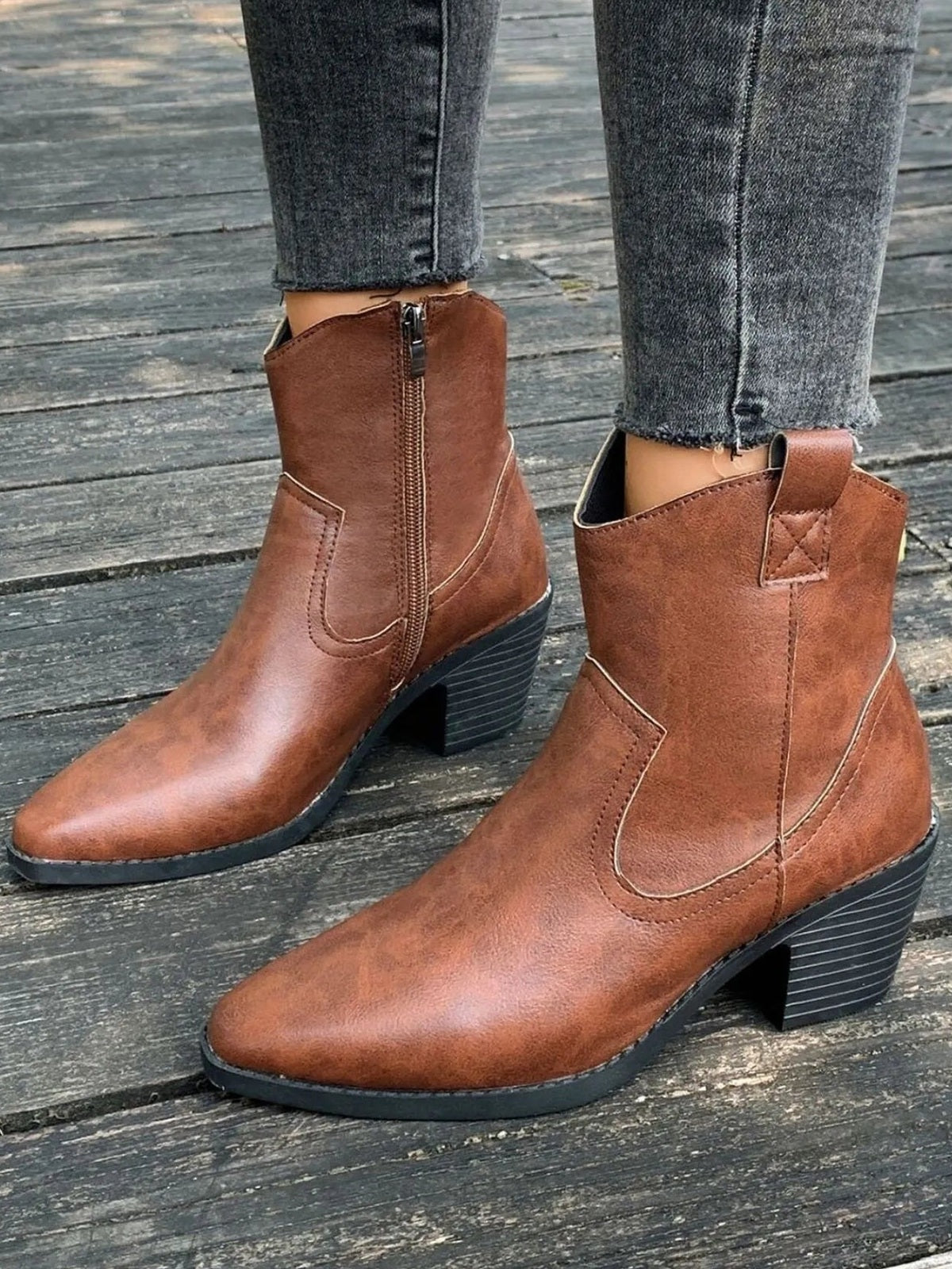Brown point-toe boots with mid block heels, side zippers, stitched panel detailing, and low-cut shafts shown on a model wearing gray jeans.
