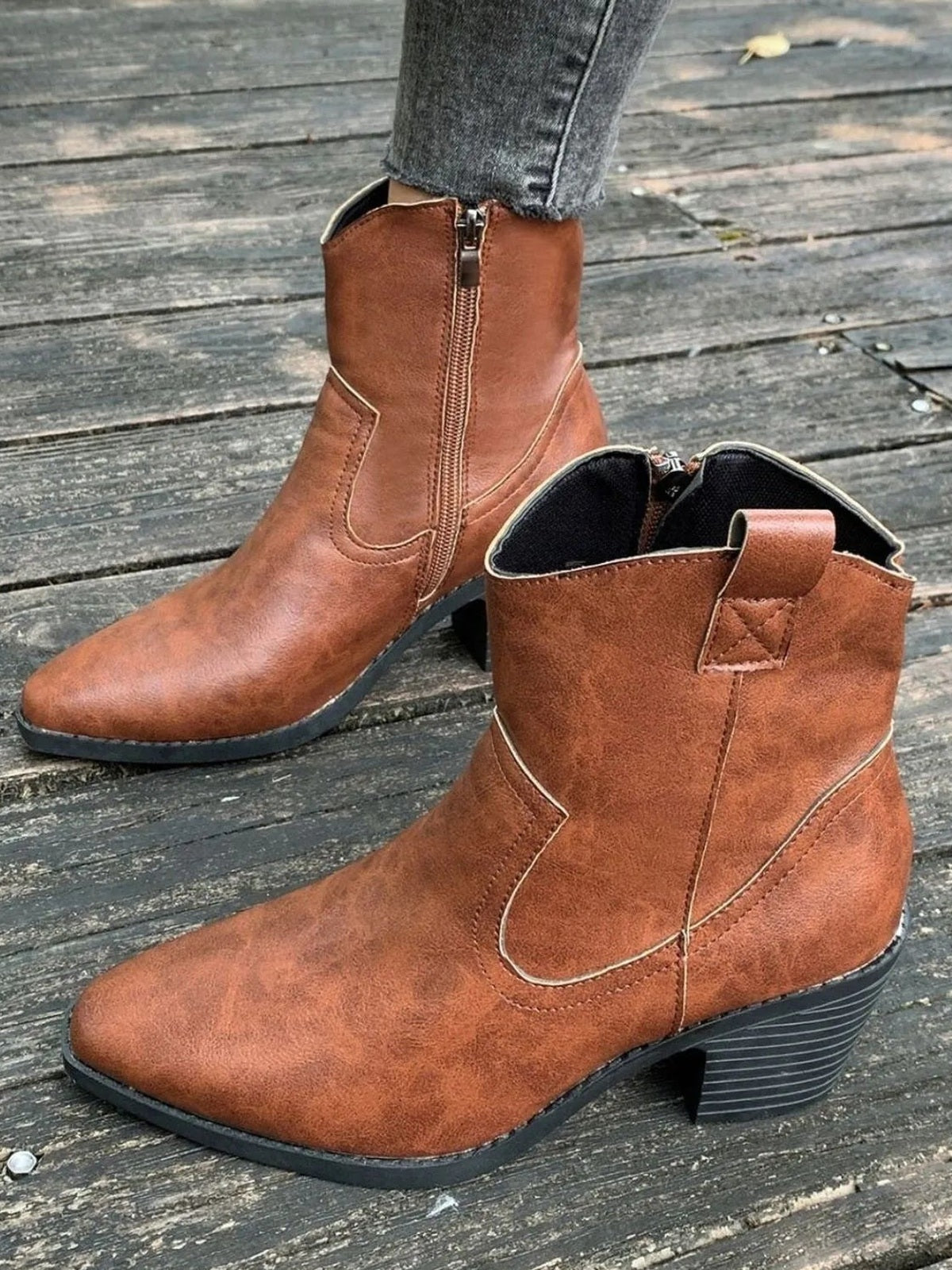 Brown pointed-toe ankle boots feature side zippers, decorative stitched panels, a sleek silhouette, and sturdy mid-height block heels.
