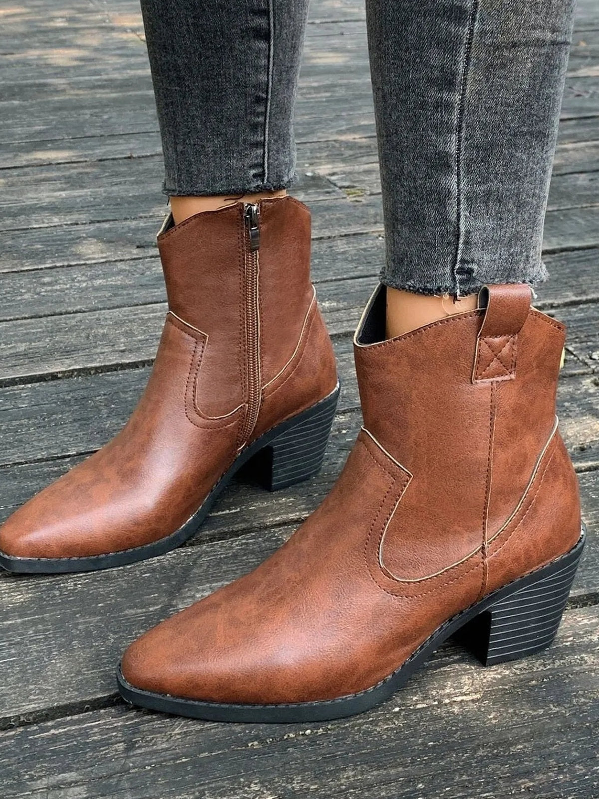 A model wears brown PU leather point-toe ankle boots with side zippers, stitched panels, and black mid-height block heels.