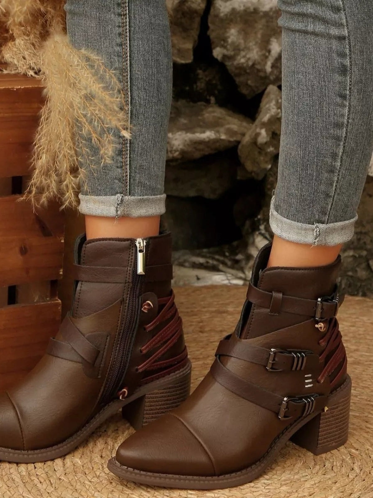 A model wears brown PU leather point-toe ankle boots with multiple buckle straps, side zippers, stitched panels, and mid-height block heels with cuffed jeans.
