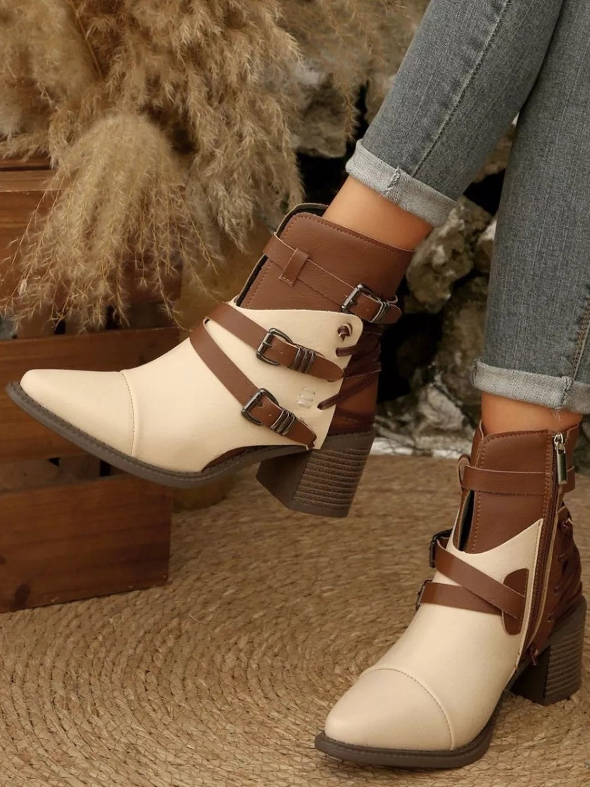 Model wears cream and brown point-toe ankle boots with multiple buckle straps, side zips, stitched panels, and mid-height block heels.