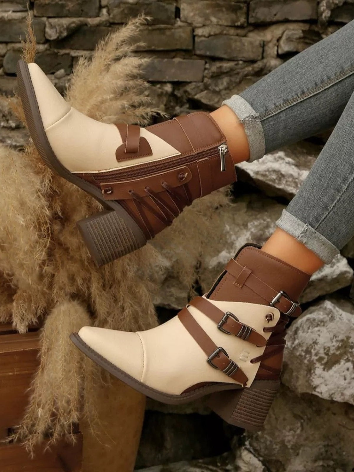 A model wears cream and brown point-toe ankle boots with multiple buckle straps, side zippers, and sturdy mid-height block heels.