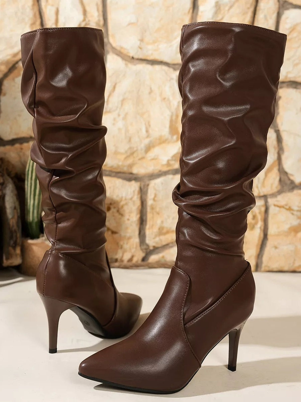 Brown PU leather knee-high boots feature pointed toes, gathered slouchy shafts, pointed-toe construction, and slim high stiletto heels.