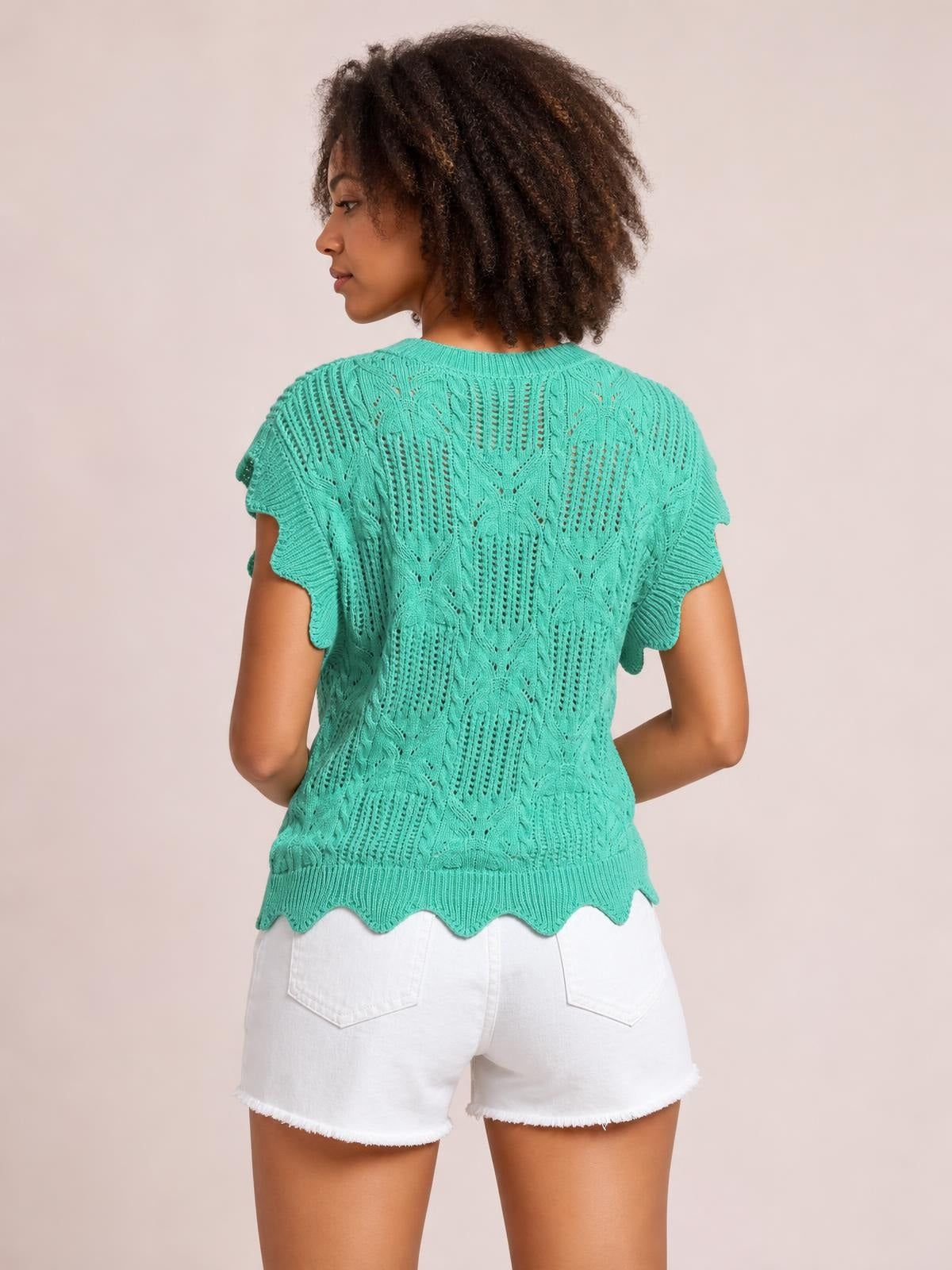 Model shown from the back wearing a turquoise pointelle knit sweater with openwork patterned texture, short sleeves, scalloped trim, and a fitted silhouette.