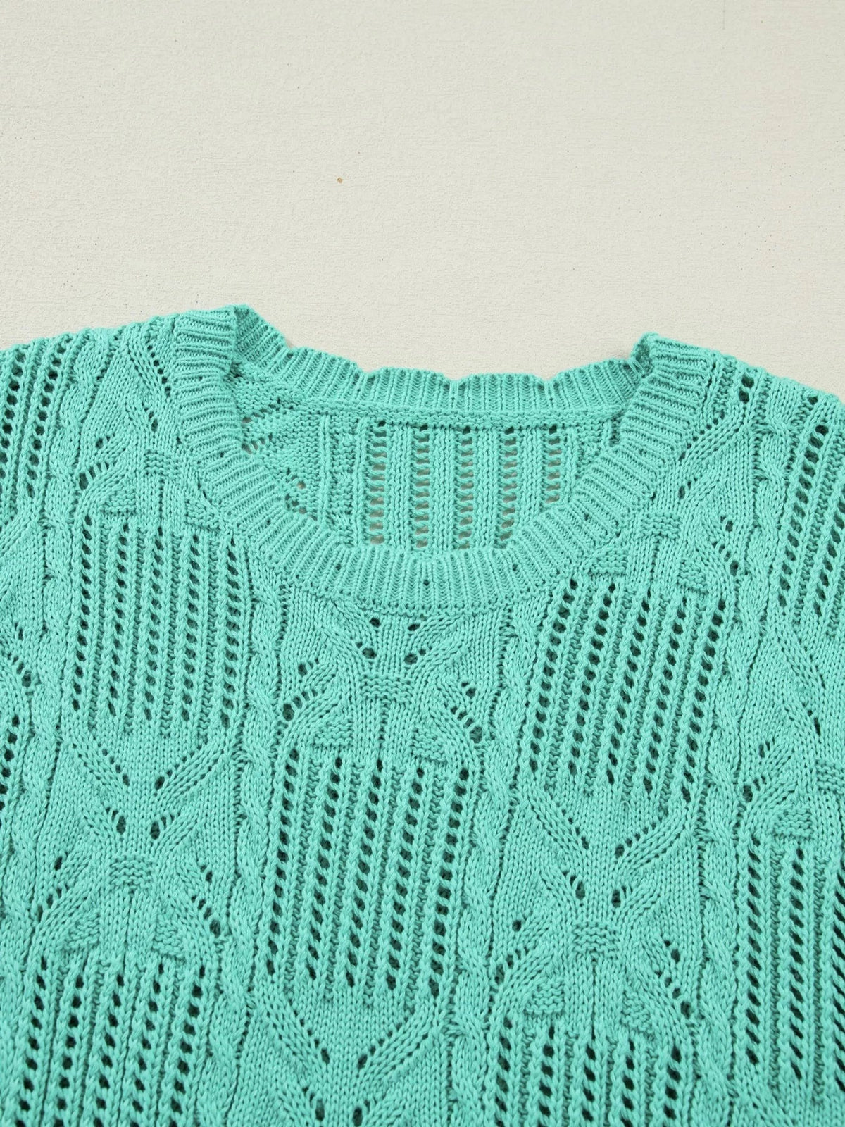 Turquoise pointelle knit sweater shown in close-up with an openwork patterned design and ribbed crew neckline.