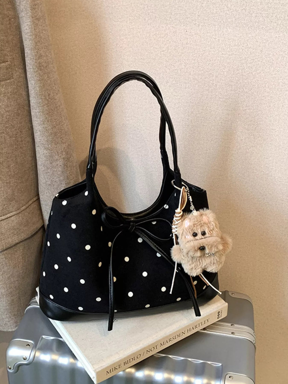 Black medium PU leather shoulder bag with white polka dots, a front bow detail, long rounded strap, and structured gusseted construction.