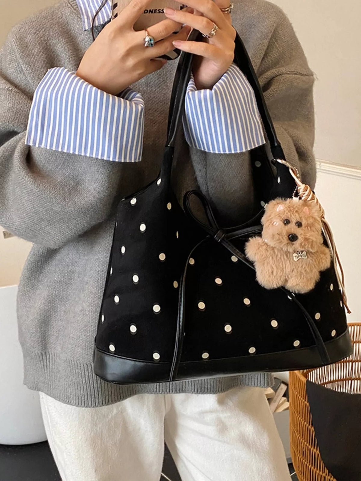 A model holds a medium black PU leather shoulder bag with white polka dots, a structured silhouette, long straps, and a prominent front bow detail.