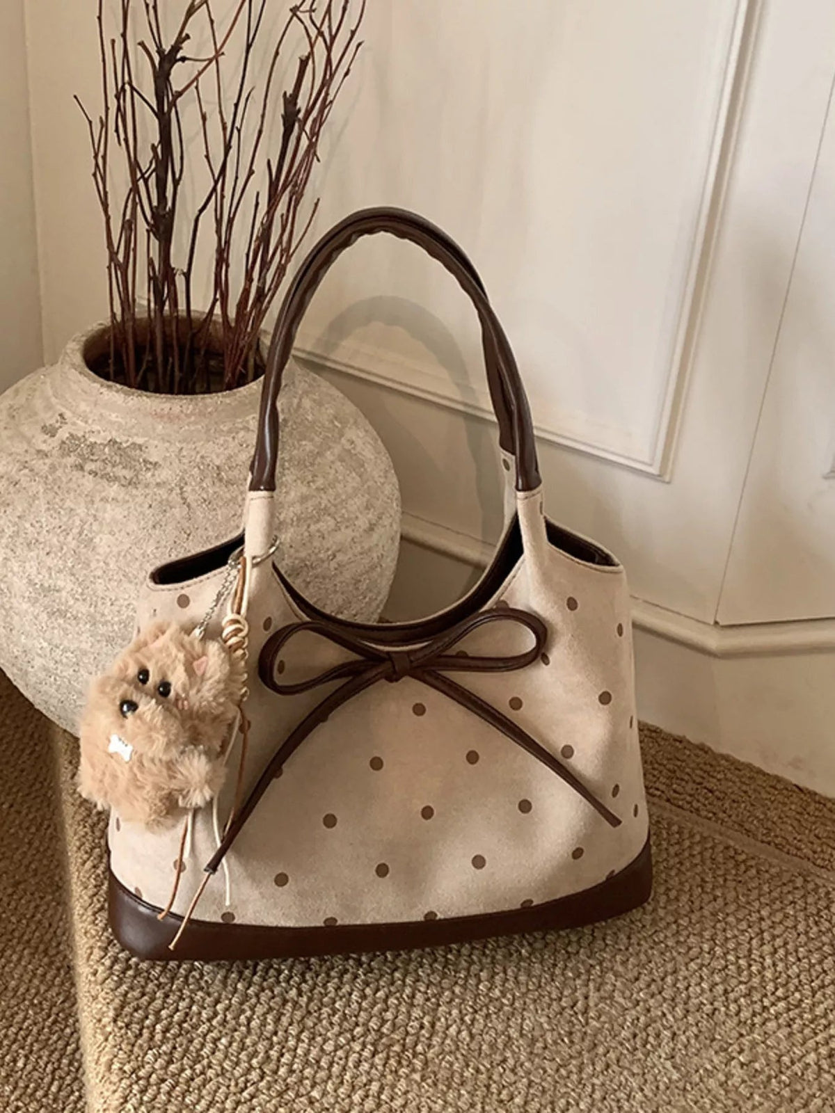 A medium cream PU leather shoulder bag with brown polka dots, contrast trim, rounded handles, a structured silhouette, and a large bow front detail.