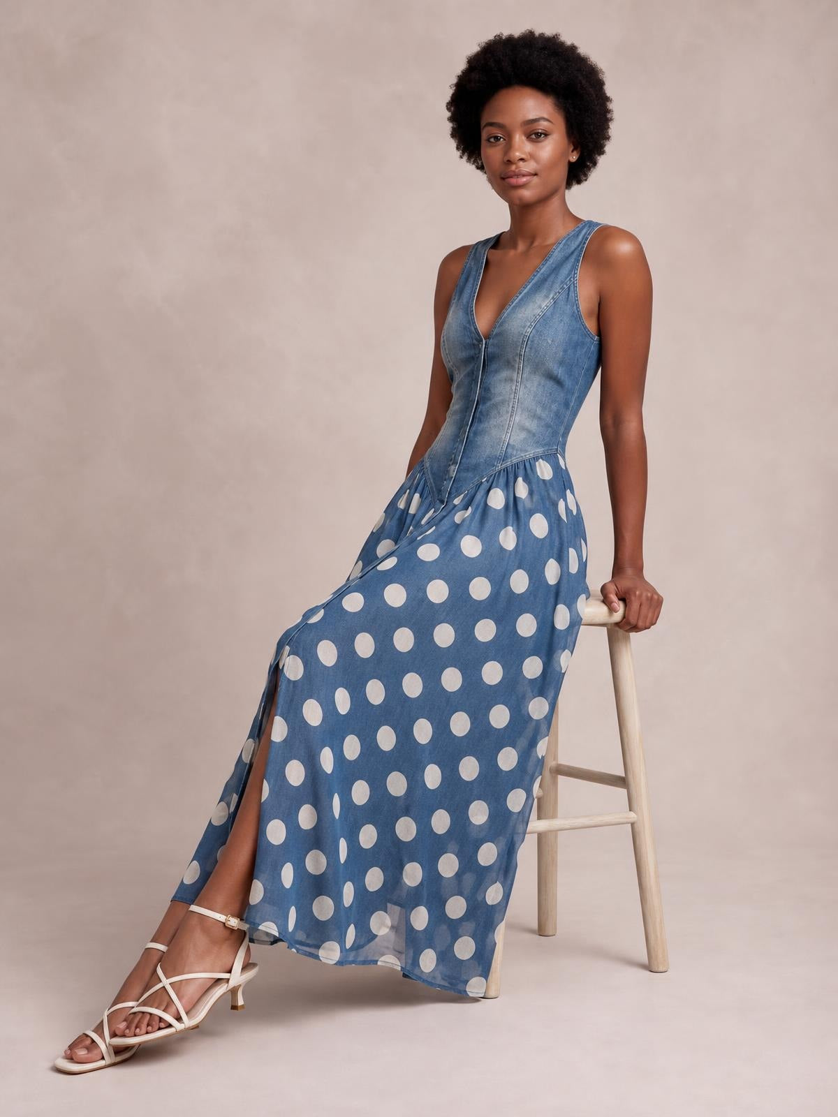 Model poses in a blue polka dot denim maxi dress with a fitted sleeveless seamed bodice and flowing full-length skirt.