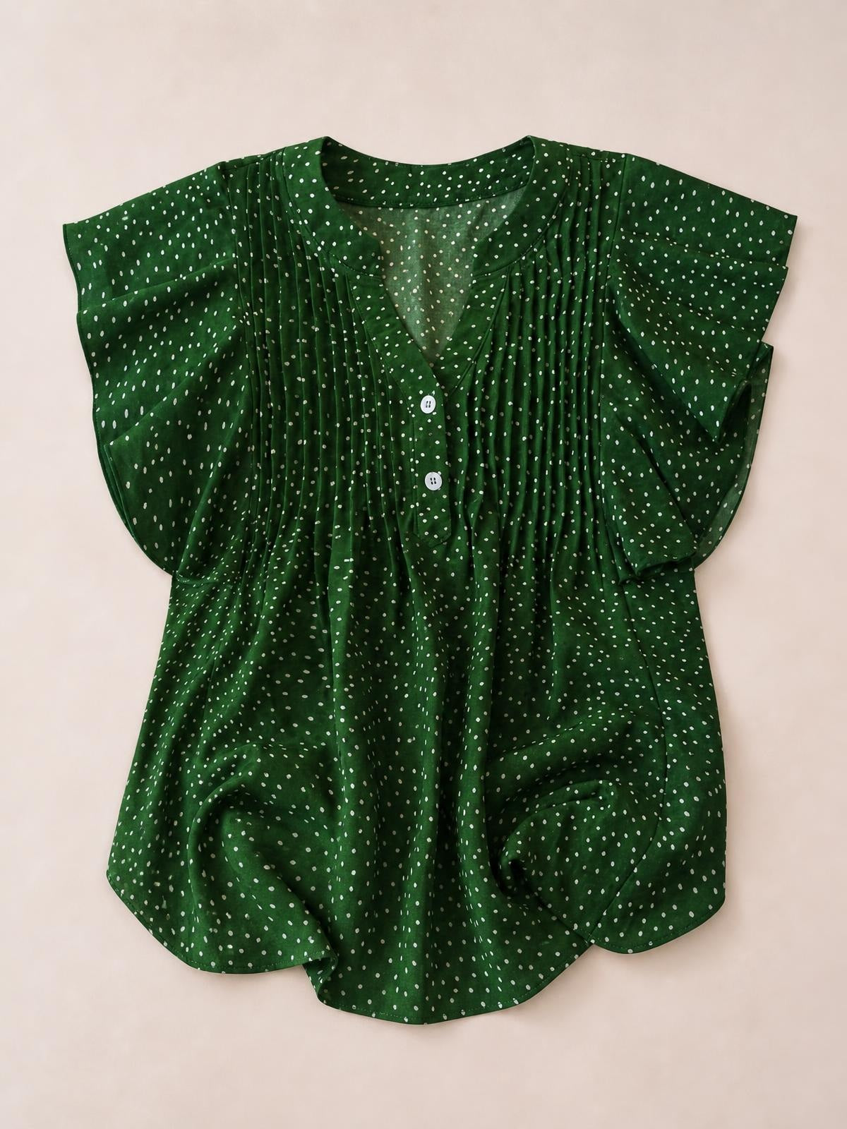 Green polka dot blouse with a notched neckline, short cap sleeves, ruched and ruffled front detailing, button closure, and a relaxed curved-hem silhouette.