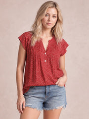 Model wearing a red polka dot blouse with a notched neckline, ruffled cap sleeves, ruched front, button closure, and relaxed silhouette.