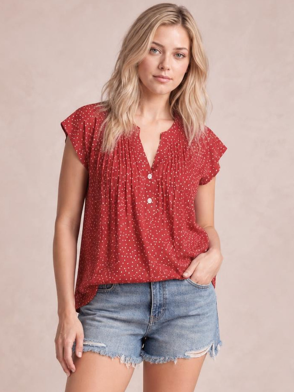 Model wearing a red polka dot blouse with a notched neckline, ruffled cap sleeves, ruched front, button closure, and relaxed silhouette.