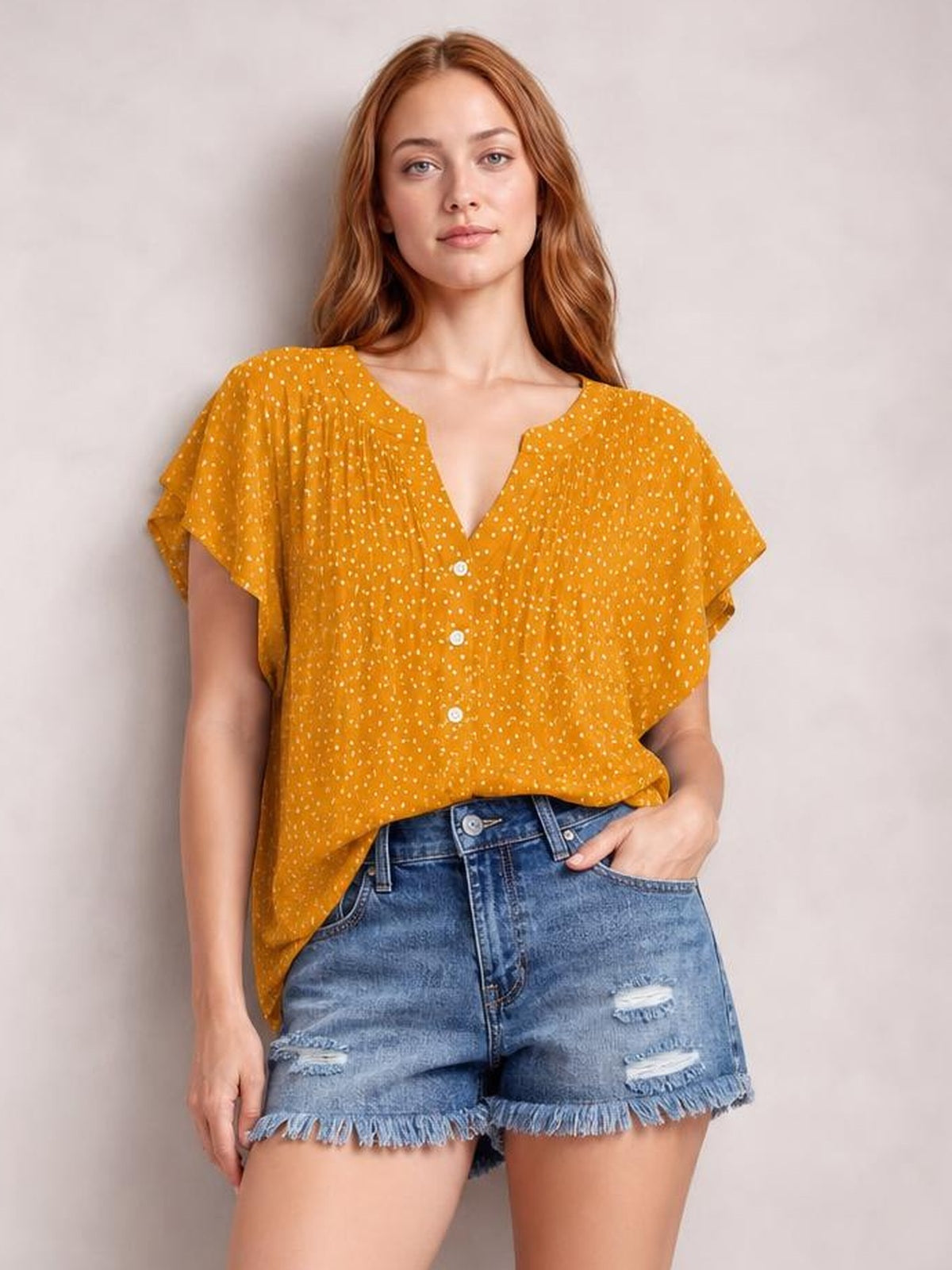 Model wears a mustard polka dot blouse with a notched neckline, ruched front, ruffled cap sleeves, button closure, and a relaxed silhouette.